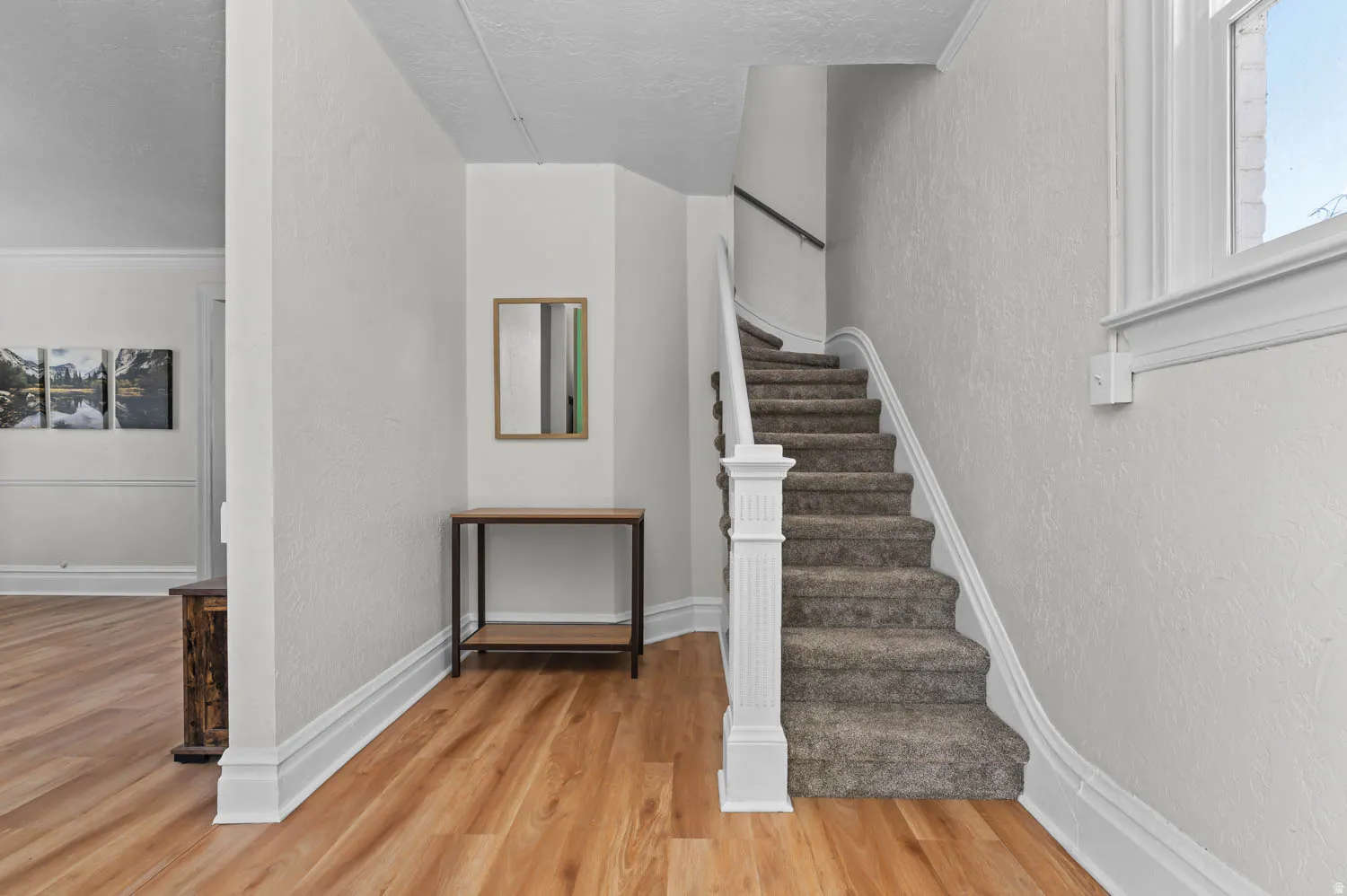 Light wood-finish flooring extending into a spacious entryway with a carpeted staircase