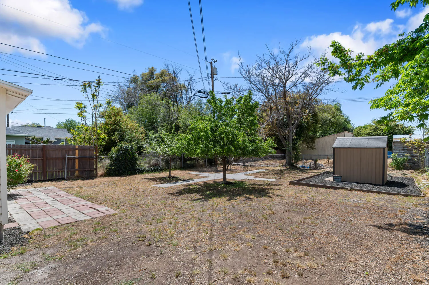 Spacious backyard featuring a brick paver patio, a utility shed with a dark rock border, and several mature trees