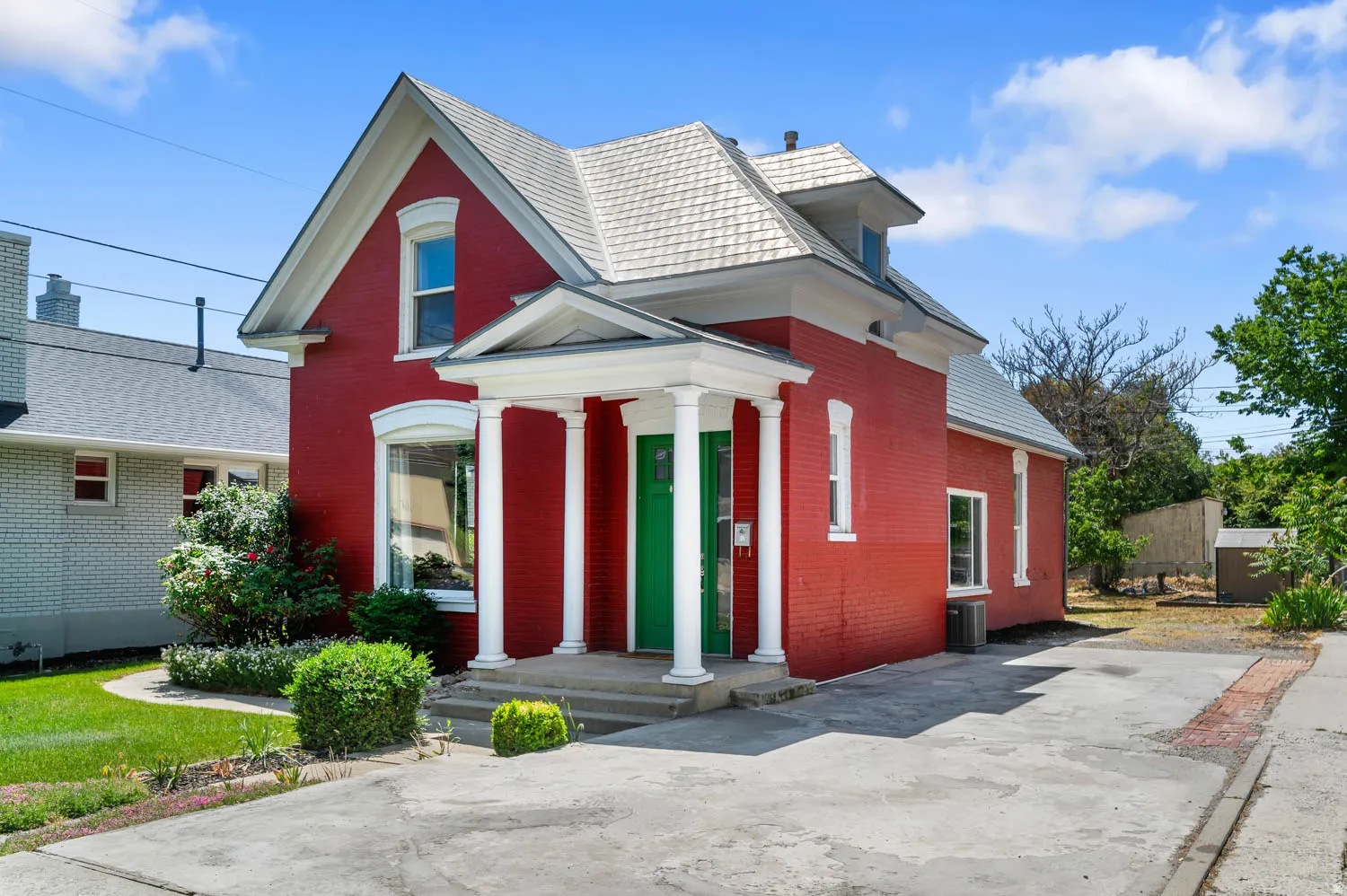 Red brick exterior with white trim details, a gray shingle roof, and a prominent front porch with white columns