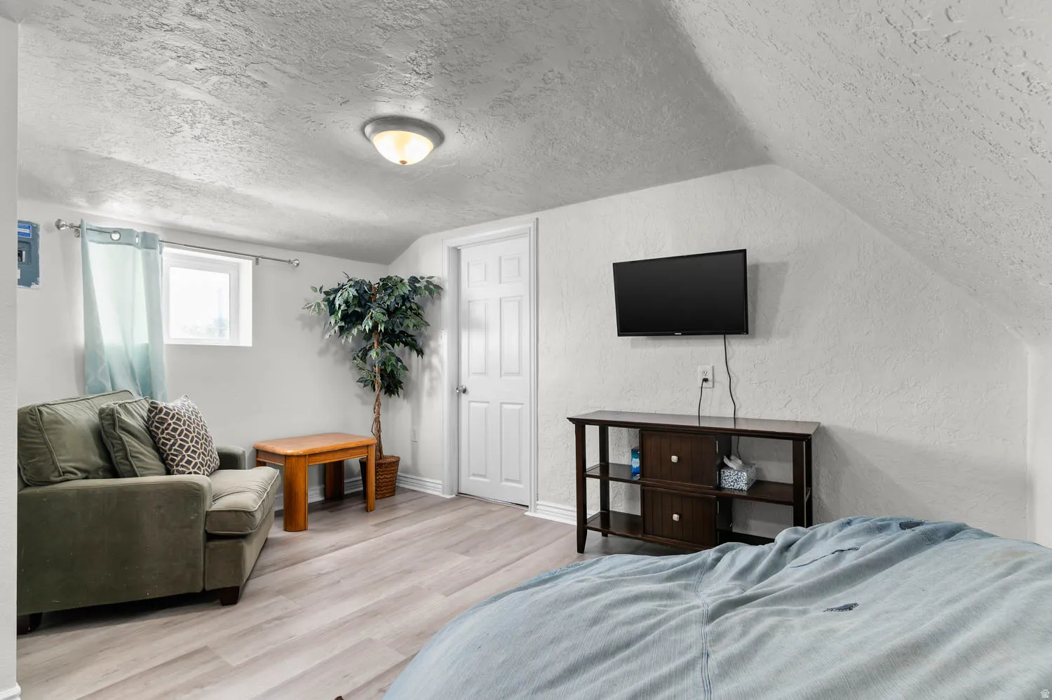 Room featuring sloped ceilings, light-toned wood-finish flooring, and a white interior door