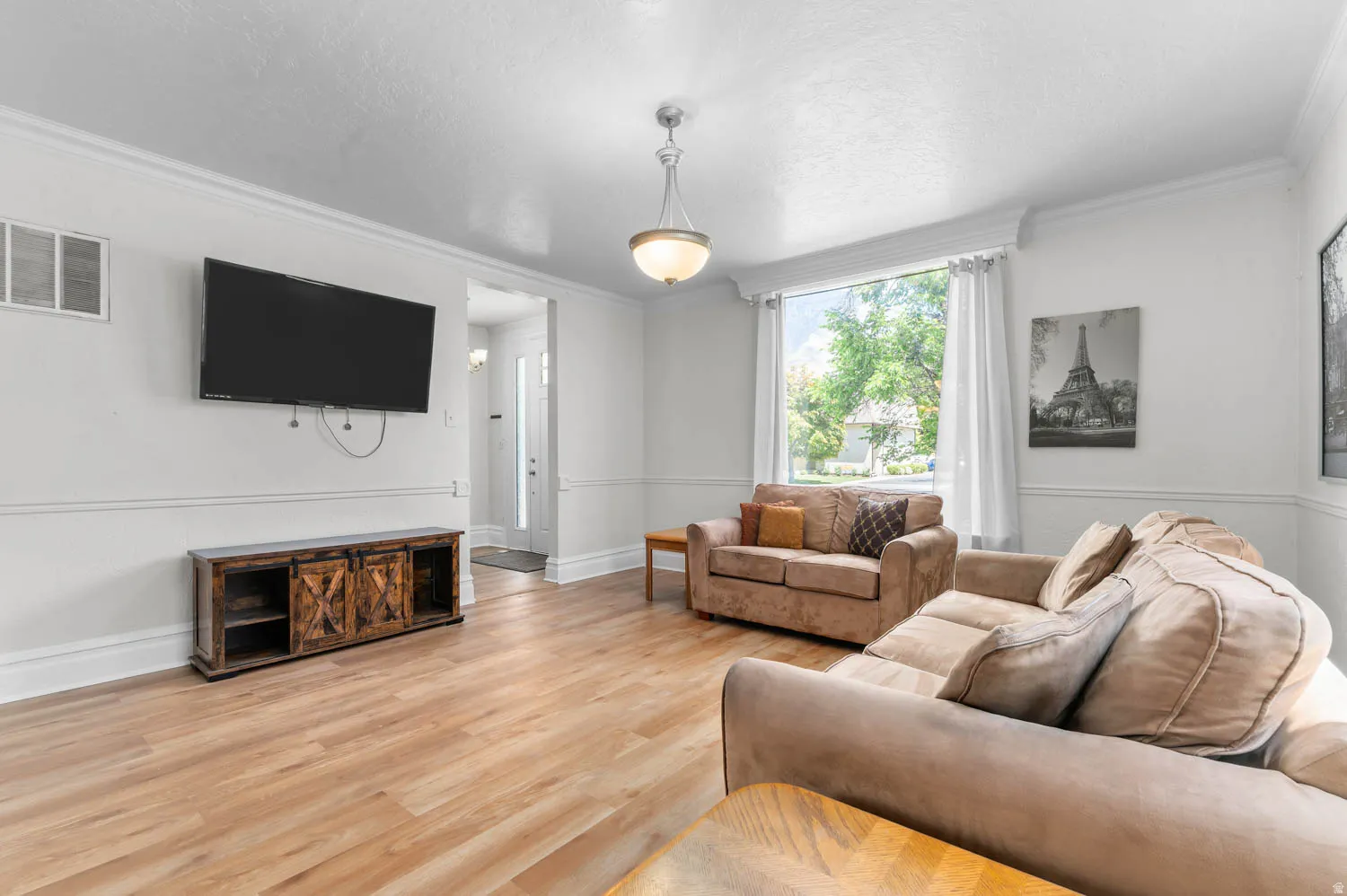 Bright living space featuring wood-finish flooring, white walls with wainscoting, and crown molding