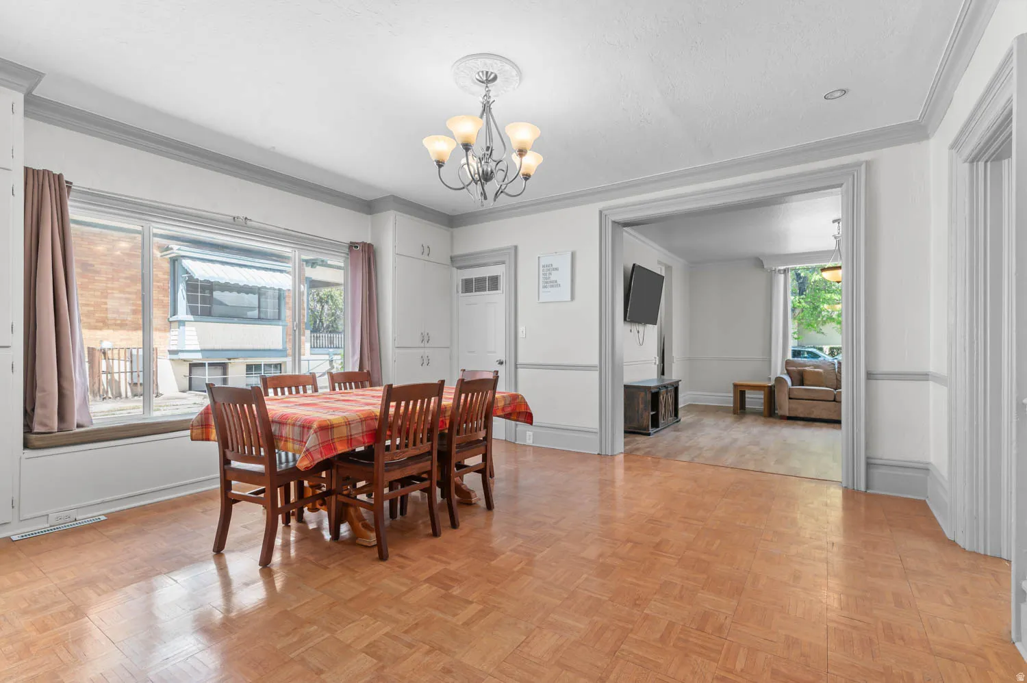 Spacious dining area featuring parquet wood-finish flooring, a contemporary chandelier, and a large window with integrated seating