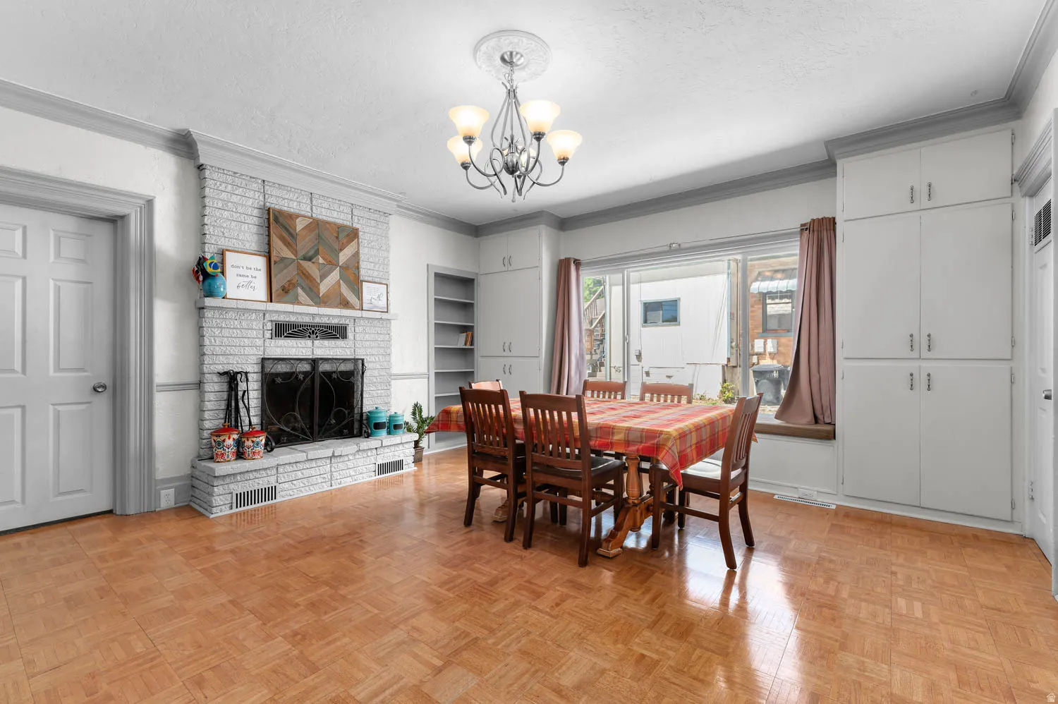 Spacious room featuring wood-finish parquet flooring and a white brick fireplace with a decorative metal screen