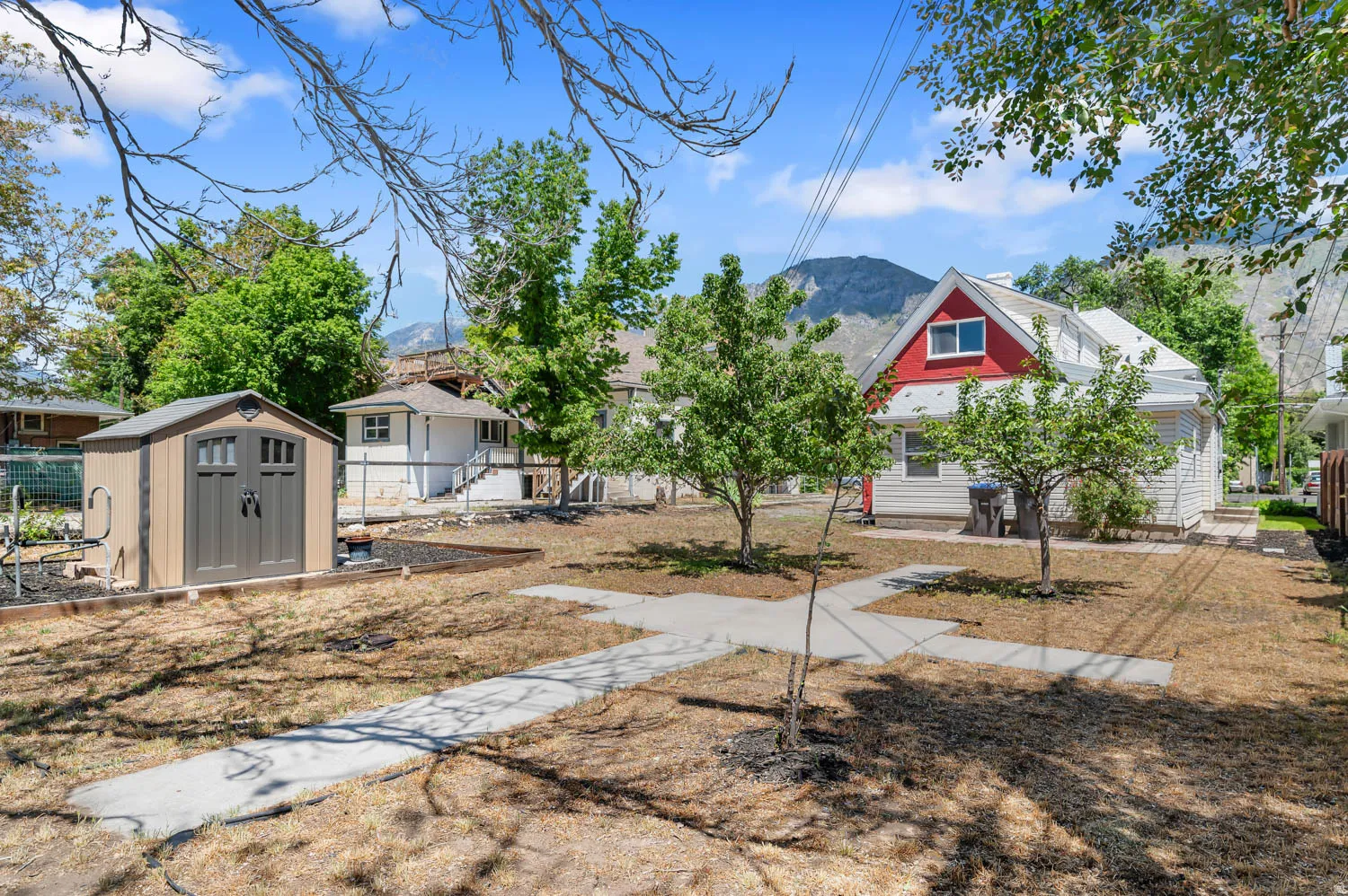 Expansive backyard featuring a storage shed with double doors, mature trees, and concrete pathways