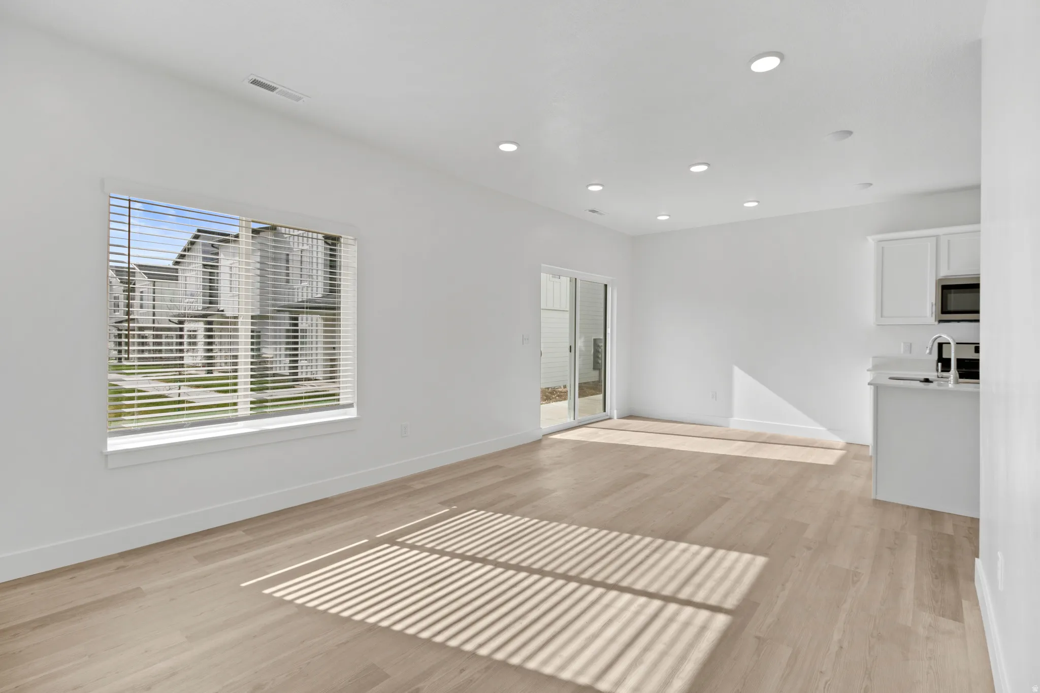 Open concept living area featuring light wood-finish flooring, recessed lighting, a large window with blinds, and a sliding glass door to the exterior