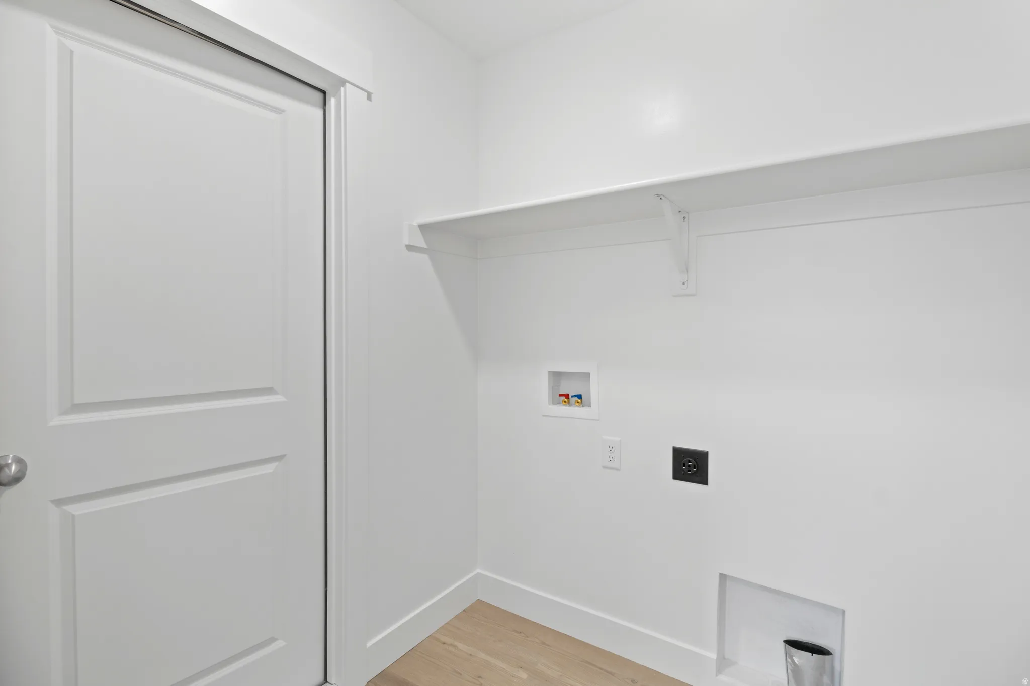 Laundry area featuring light wood-finish flooring, white baseboards, and a built-in shelving unit