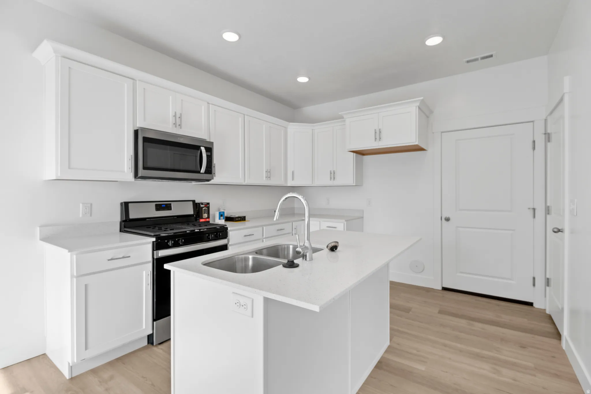Modern kitchen featuring an island with a double basin sink, white cabinetry with crown molding, stainless steel appliances, recessed lighting, and wood-finish flooring