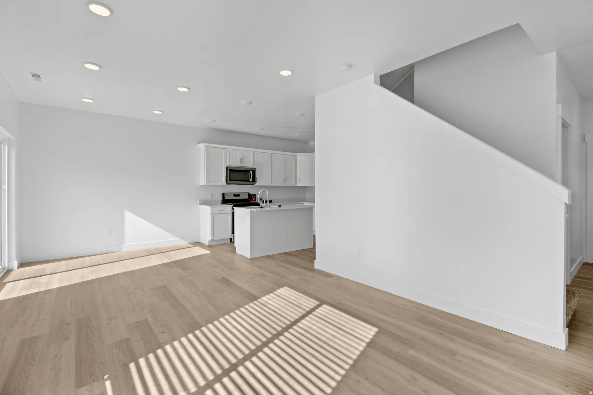 Open-concept main level featuring wood-finish flooring, recessed lighting, a sliding glass door, white cabinetry, and an integrated kitchen island with a sink