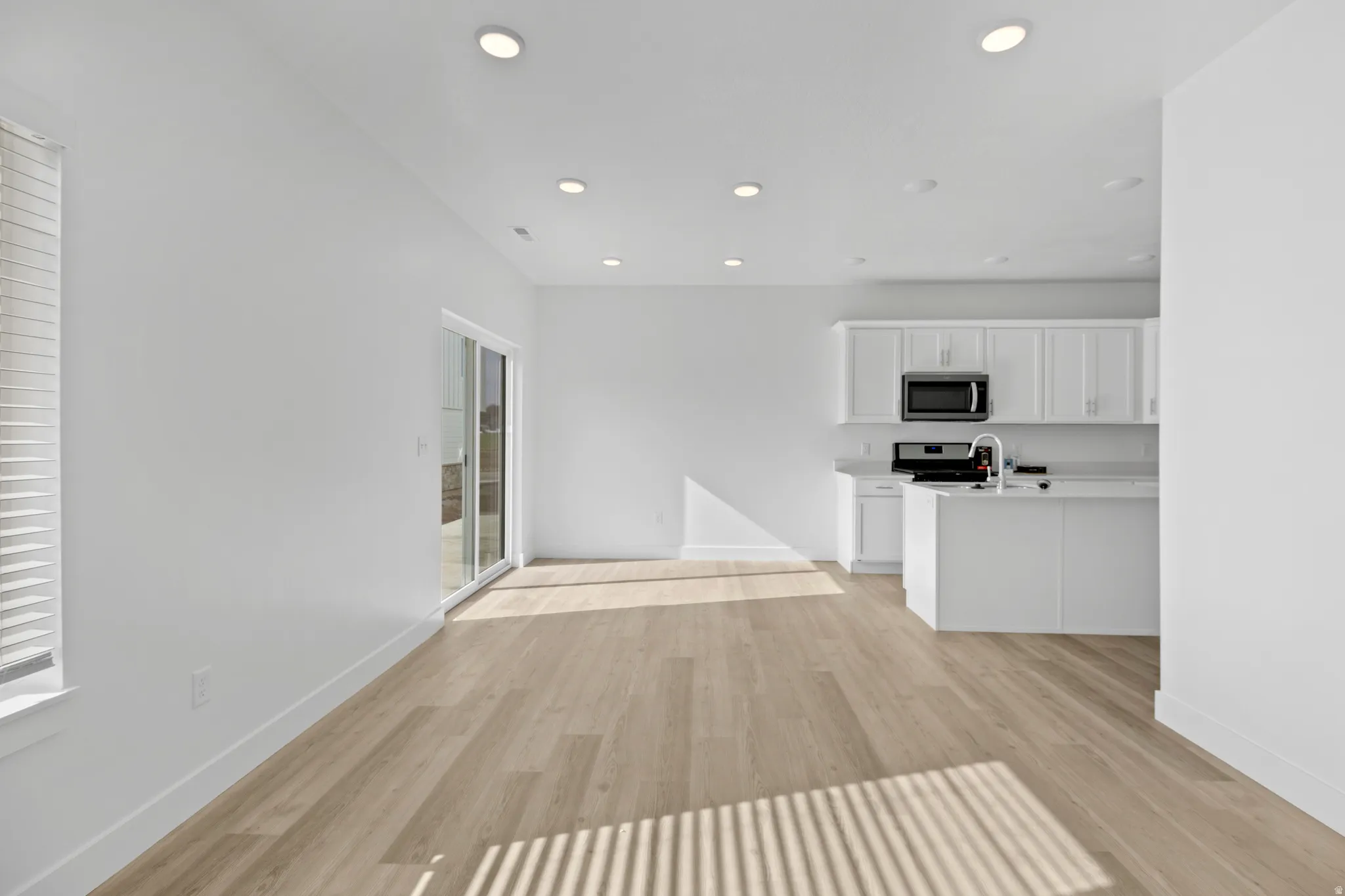Open-concept living area featuring light wood-finish flooring, recessed lighting, and a modern kitchen