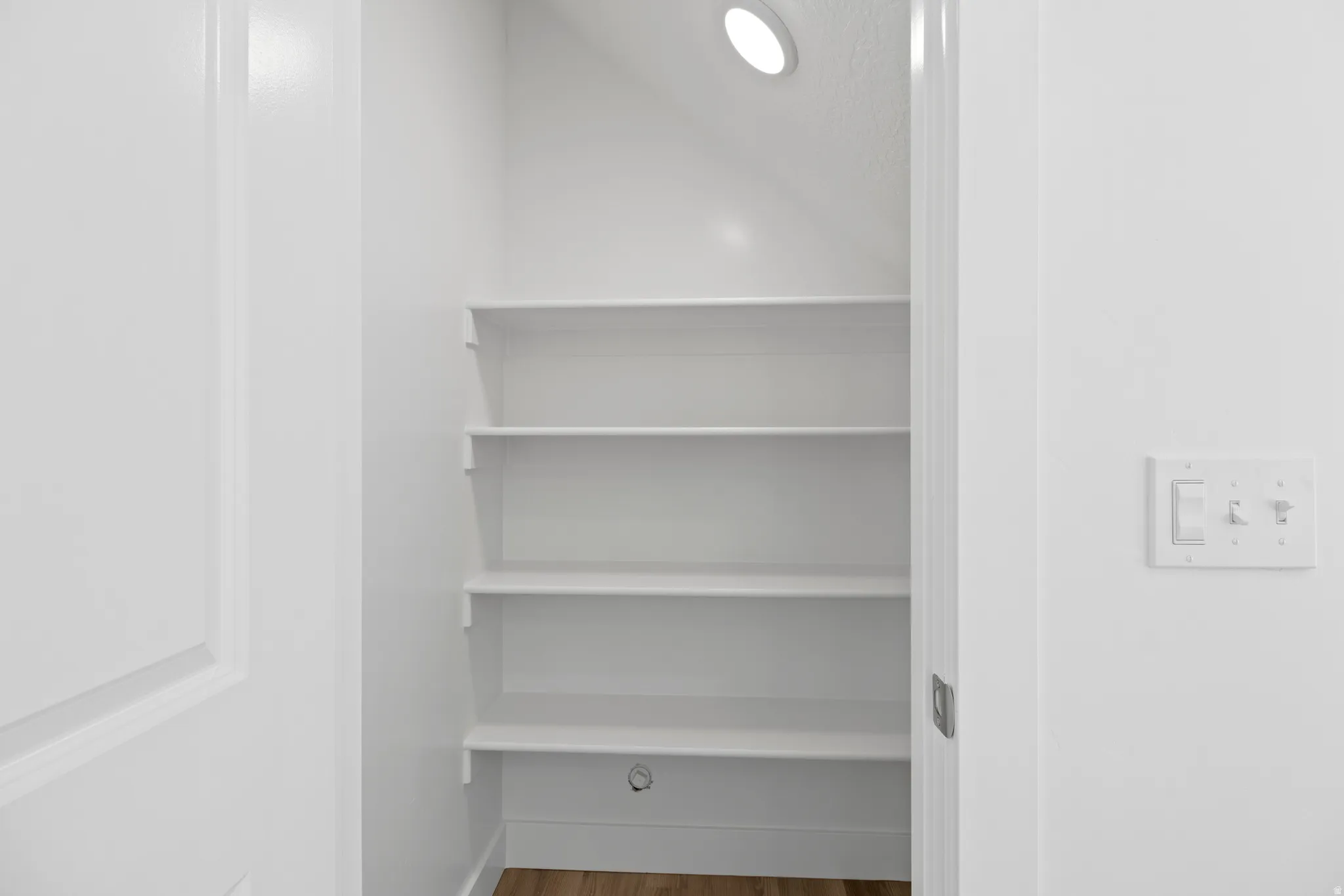 Interior pantry with five white shelves, recessed ceiling lighting, and wood-finish flooring