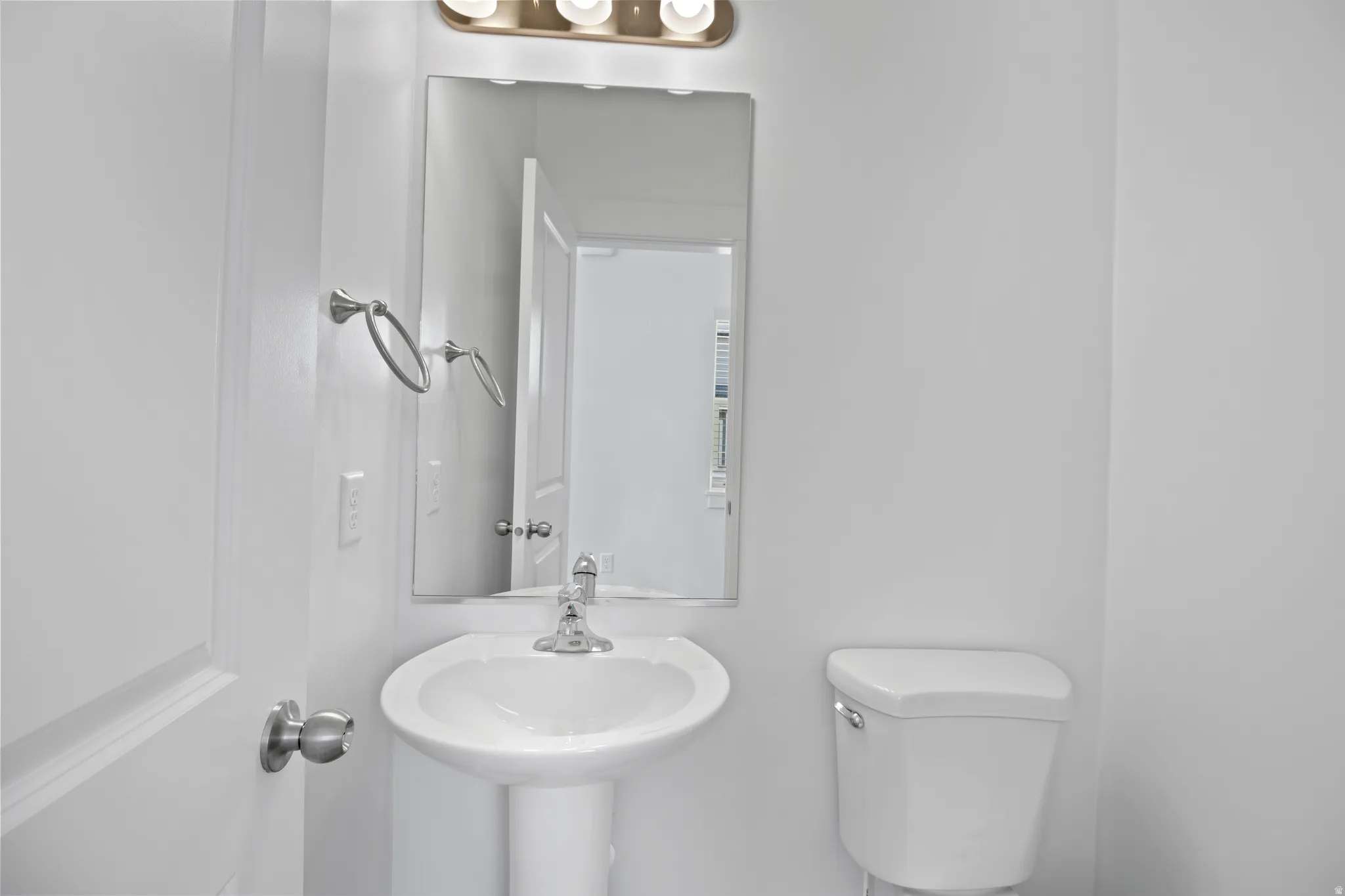 Bathroom featuring a pedestal sink with chrome faucet, mirror, and overhead vanity lighting