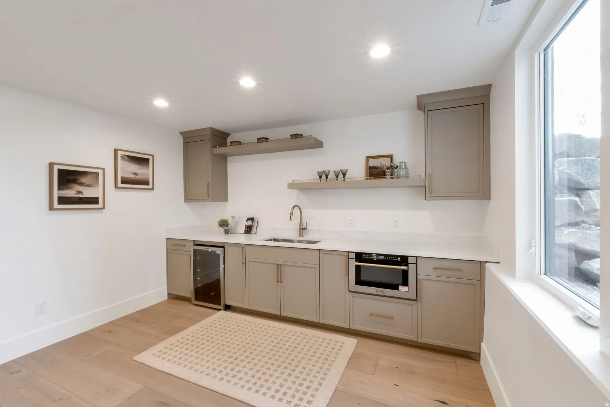 Kitchenette featuring light-toned cabinetry, a built-in microwave, under-counter beverage refrigerator, and a stainless steel sink with a single-handle faucet