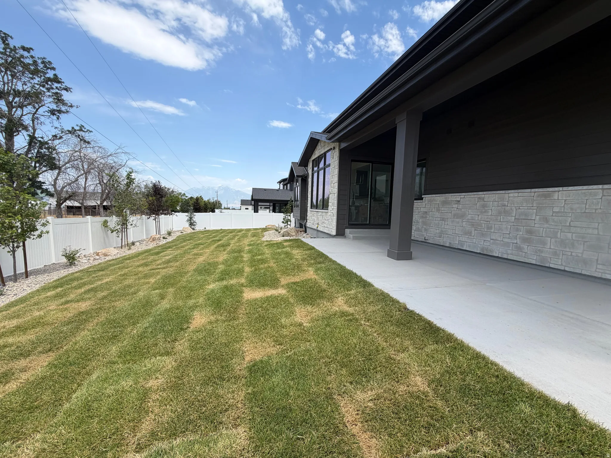 Modern exterior featuring dark siding, light-toned stone accents, and a covered concrete patio