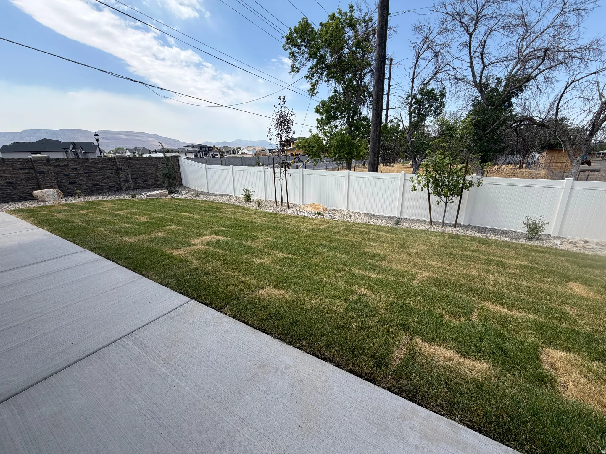 Spacious backyard featuring a concrete patio, a green lawn, and a white vinyl privacy fence