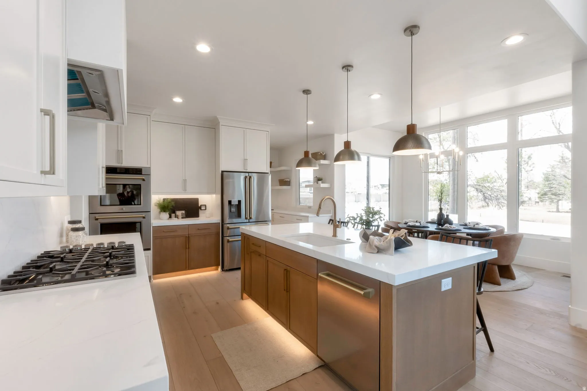 Gourmet kitchen with a large central island, white countertops, integrated stainless steel appliances, and wood-finish flooring