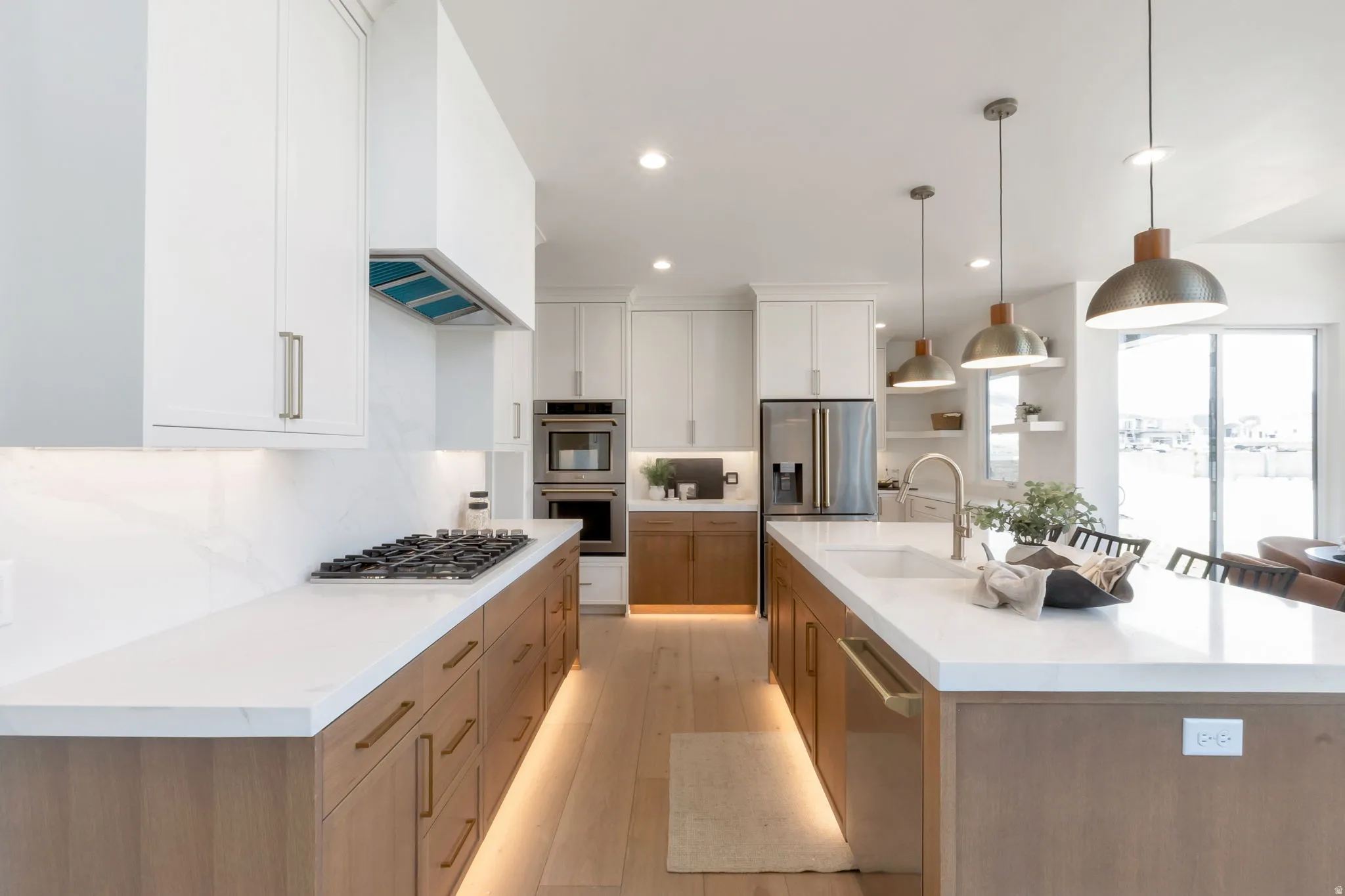 Modern kitchen featuring two-tone cabinetry, a gas cooktop, built-in double ovens, and a large center island with an undermount sink and pendant lighting
