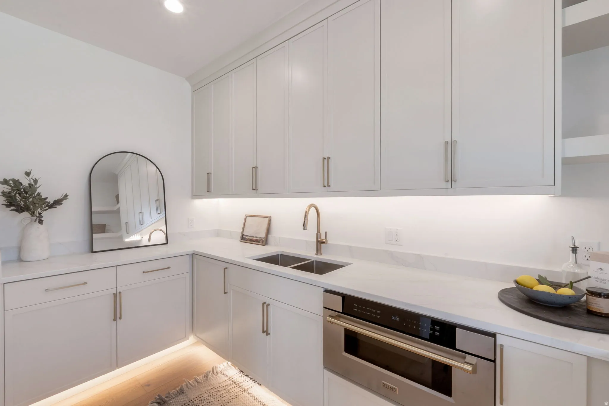 Light-toned cabinetry with brass hardware, undermount double sink with brass faucet, built-in microwave, and marble-finish countertops