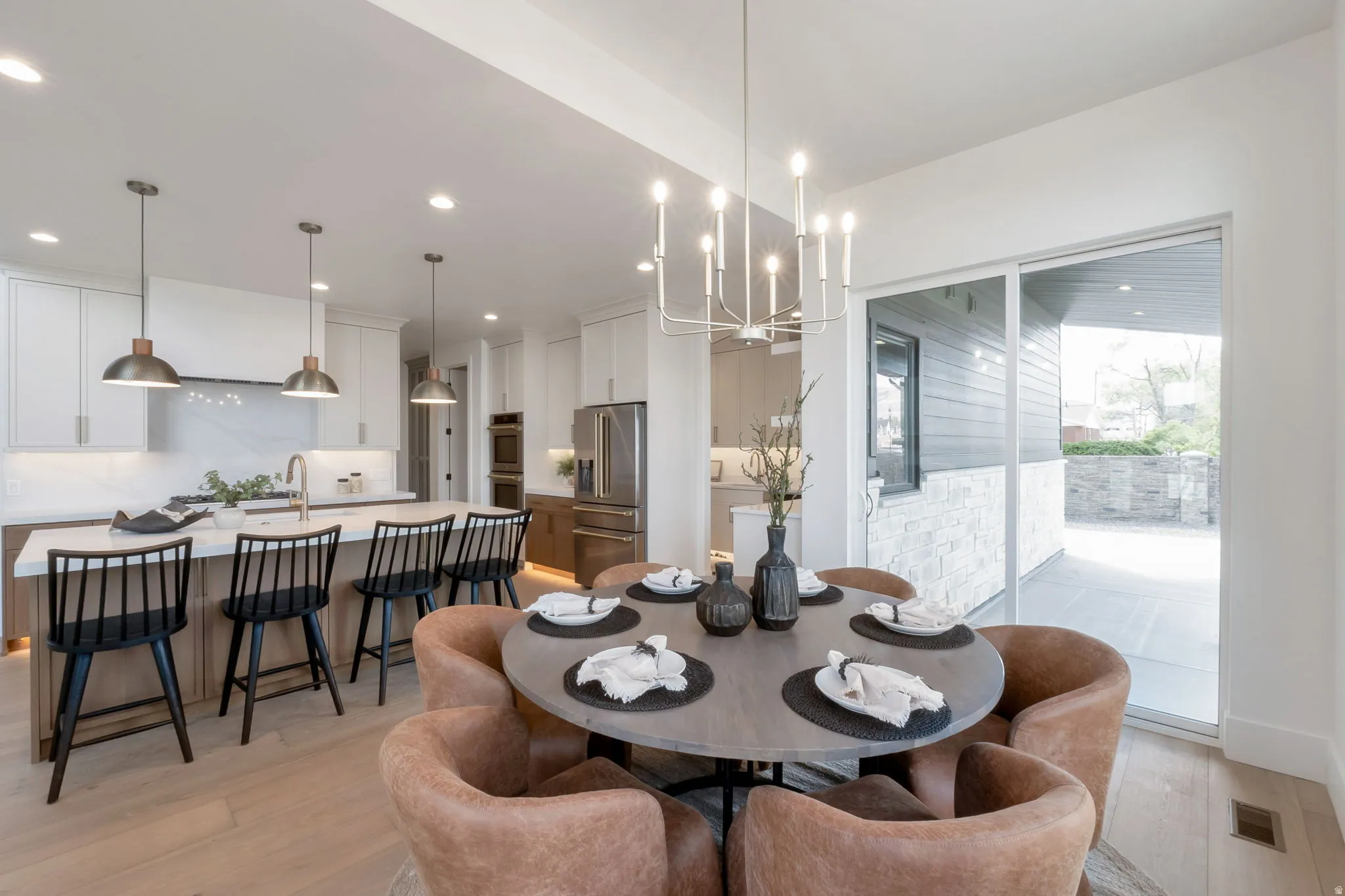 Open-concept dining area featuring a modern chandelier, wood-finish flooring, and a sliding glass door providing access to an exterior patio