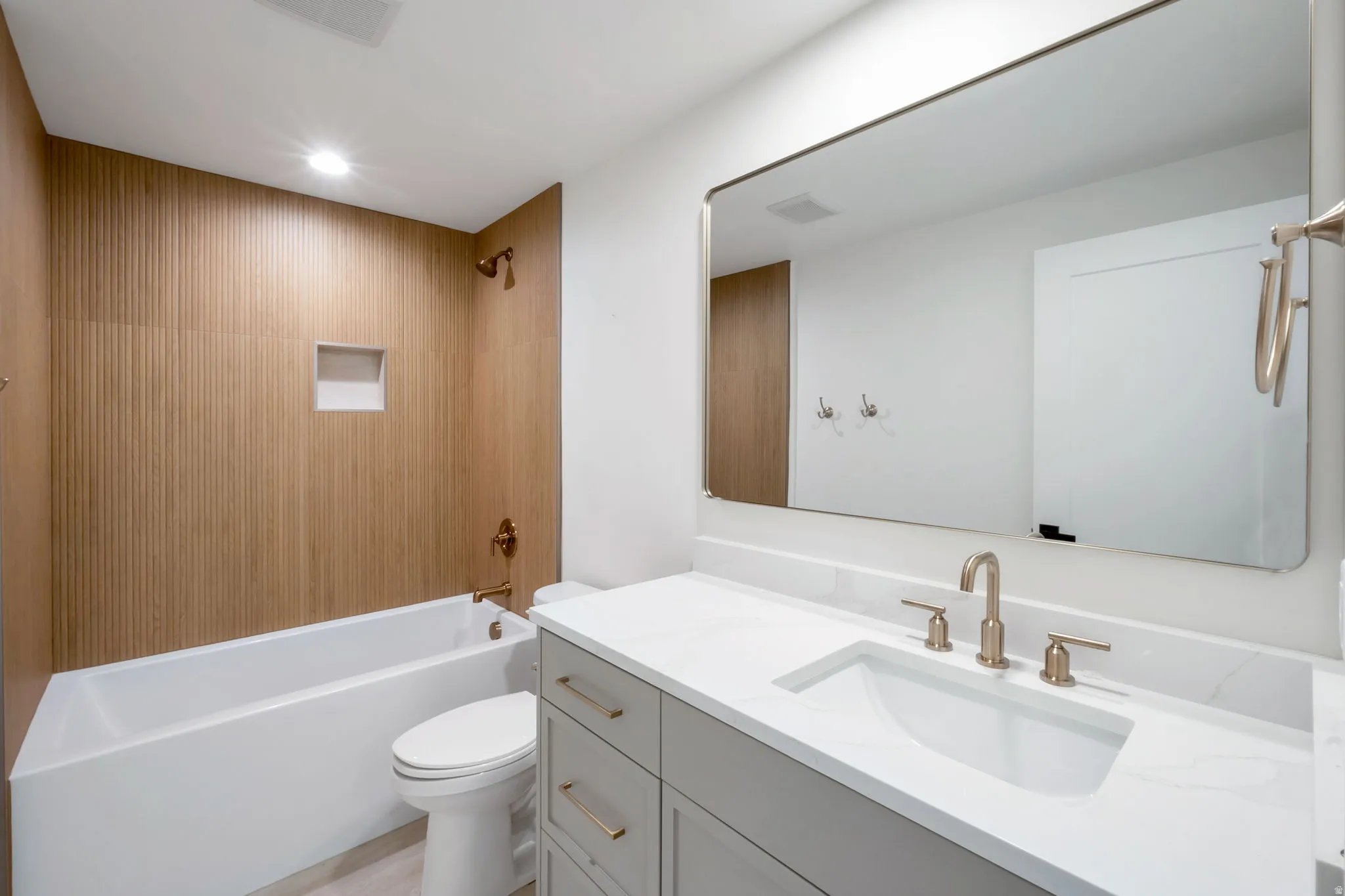 Bathroom featuring a white soaking tub with wood-finish tile surround, integrated shower niche, and bronze fixtures