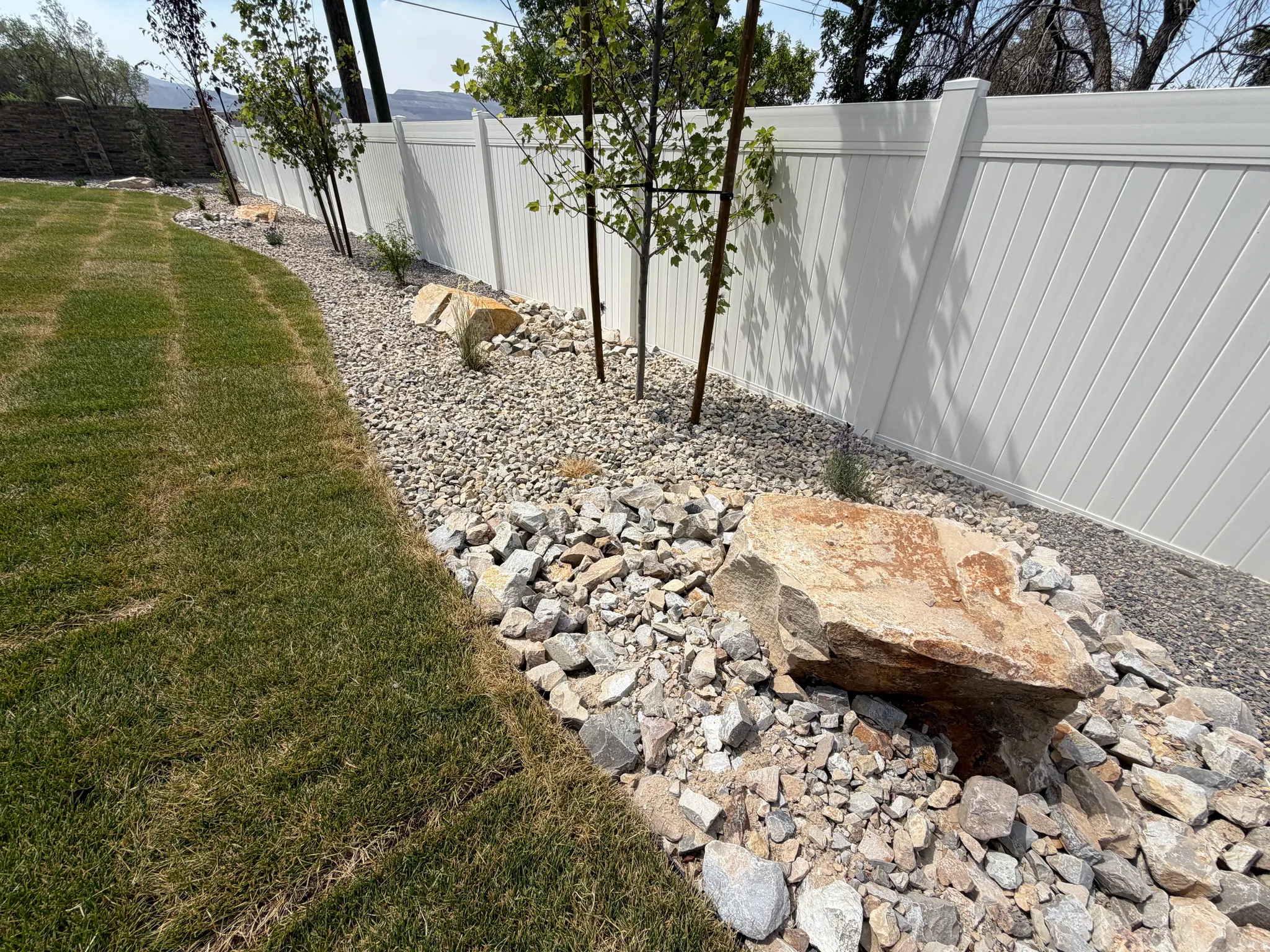 Expansive lawn area bordered by a rock-lined garden bed featuring mature trees and large natural boulders