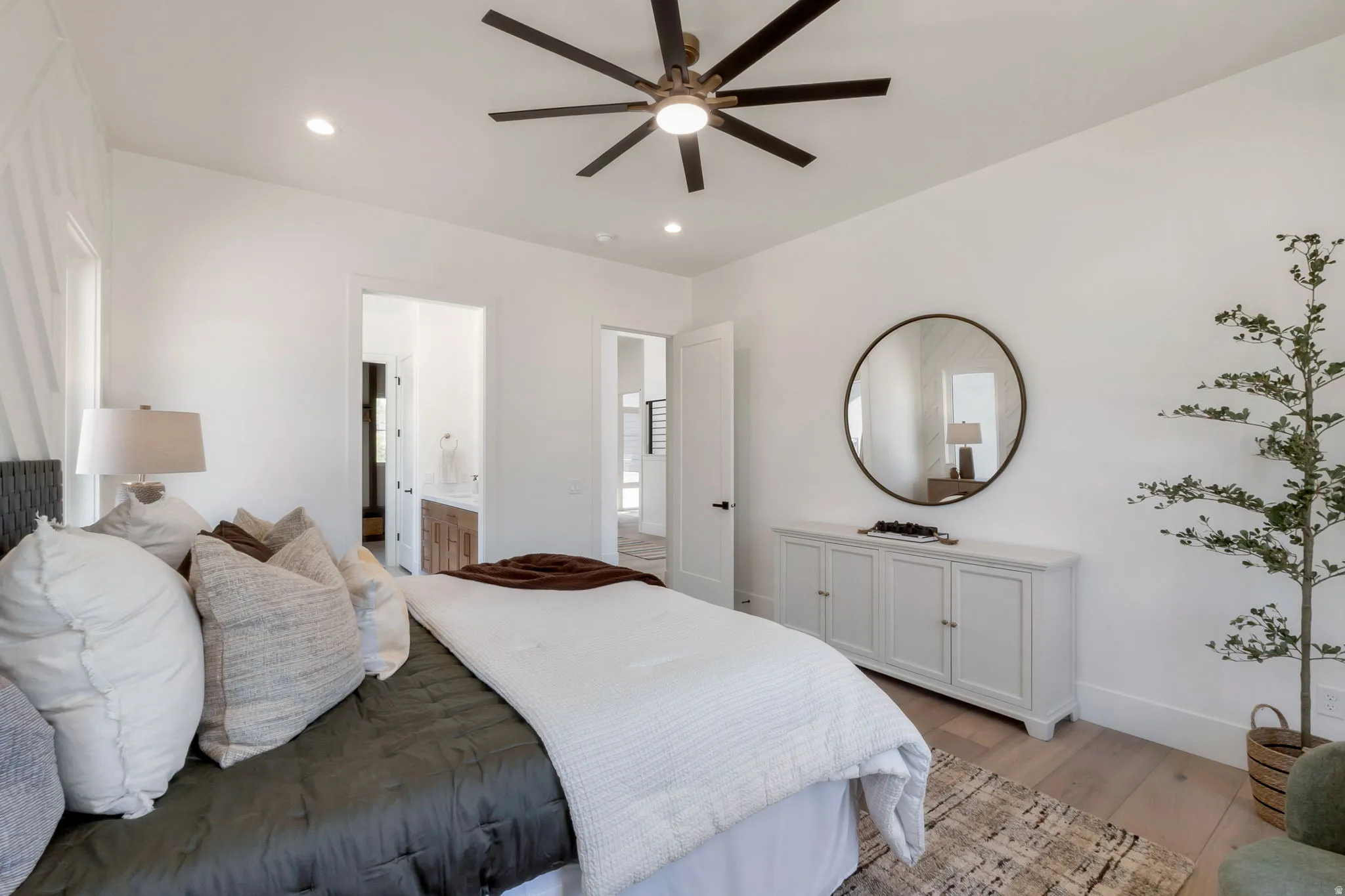Spacious bedroom with recessed lighting and a ceiling fan, featuring light wood-finish flooring and a custom accent wall