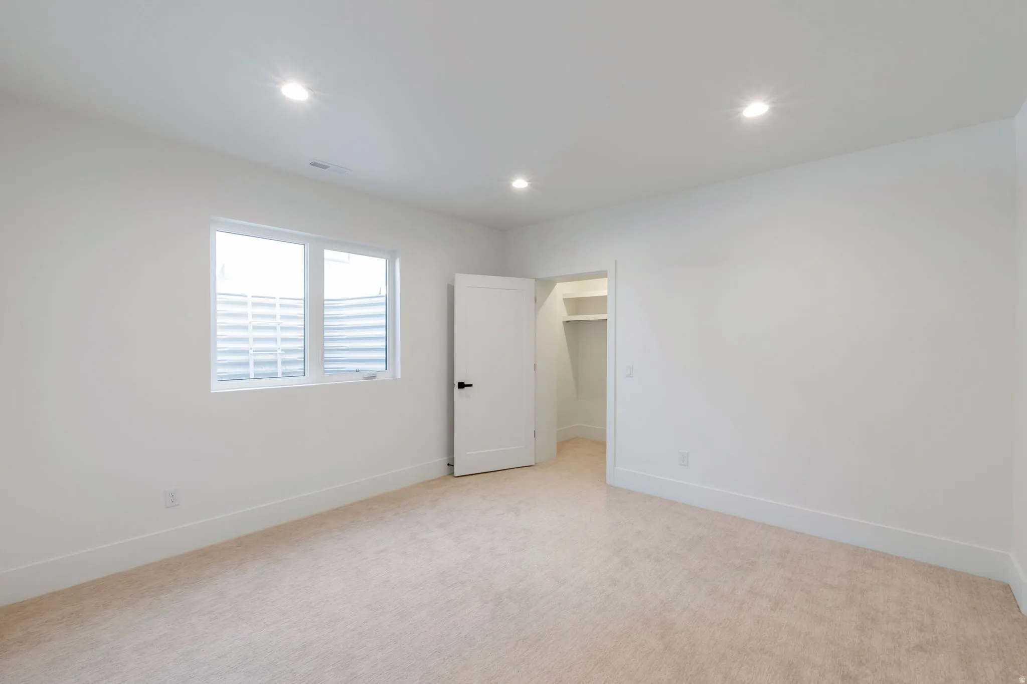 Carpeted room featuring a white interior door, a window with horizontal blinds, recessed lighting, and a closet with built-in shelving