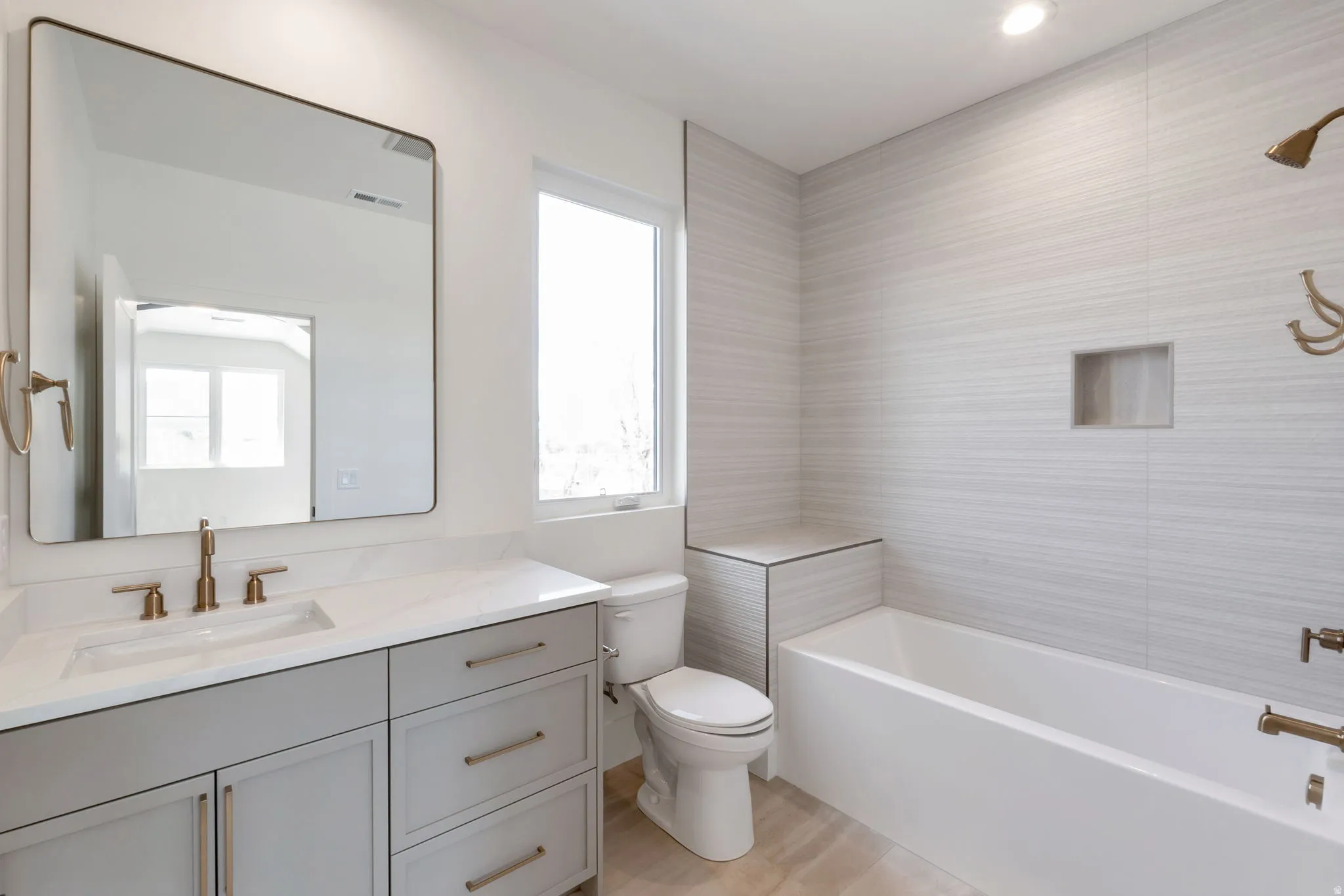 Bathroom featuring a single vanity with light grey cabinetry, white countertop, and gold-finish fixtures