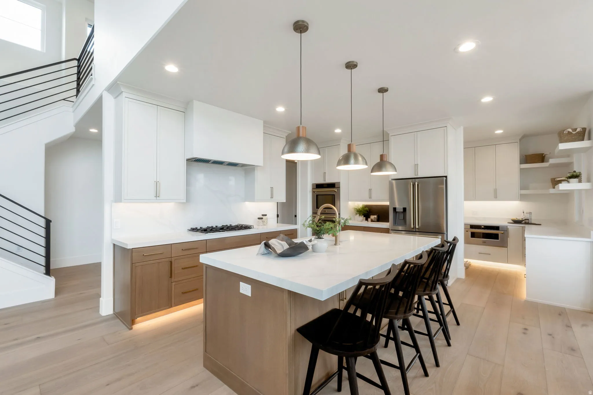 Gourmet kitchen with a large central island, light wood-finish flooring, white upper cabinetry, natural wood-tone lower cabinetry, and stainless steel appliances