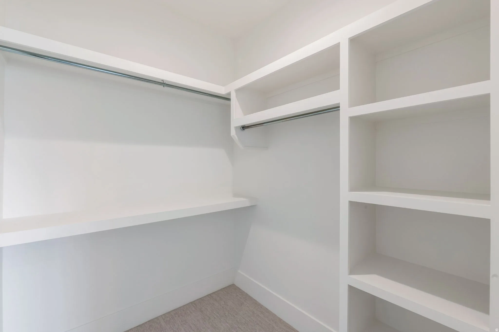 Built-in closet organization featuring white shelving, hanging rods, and light-colored carpet flooring