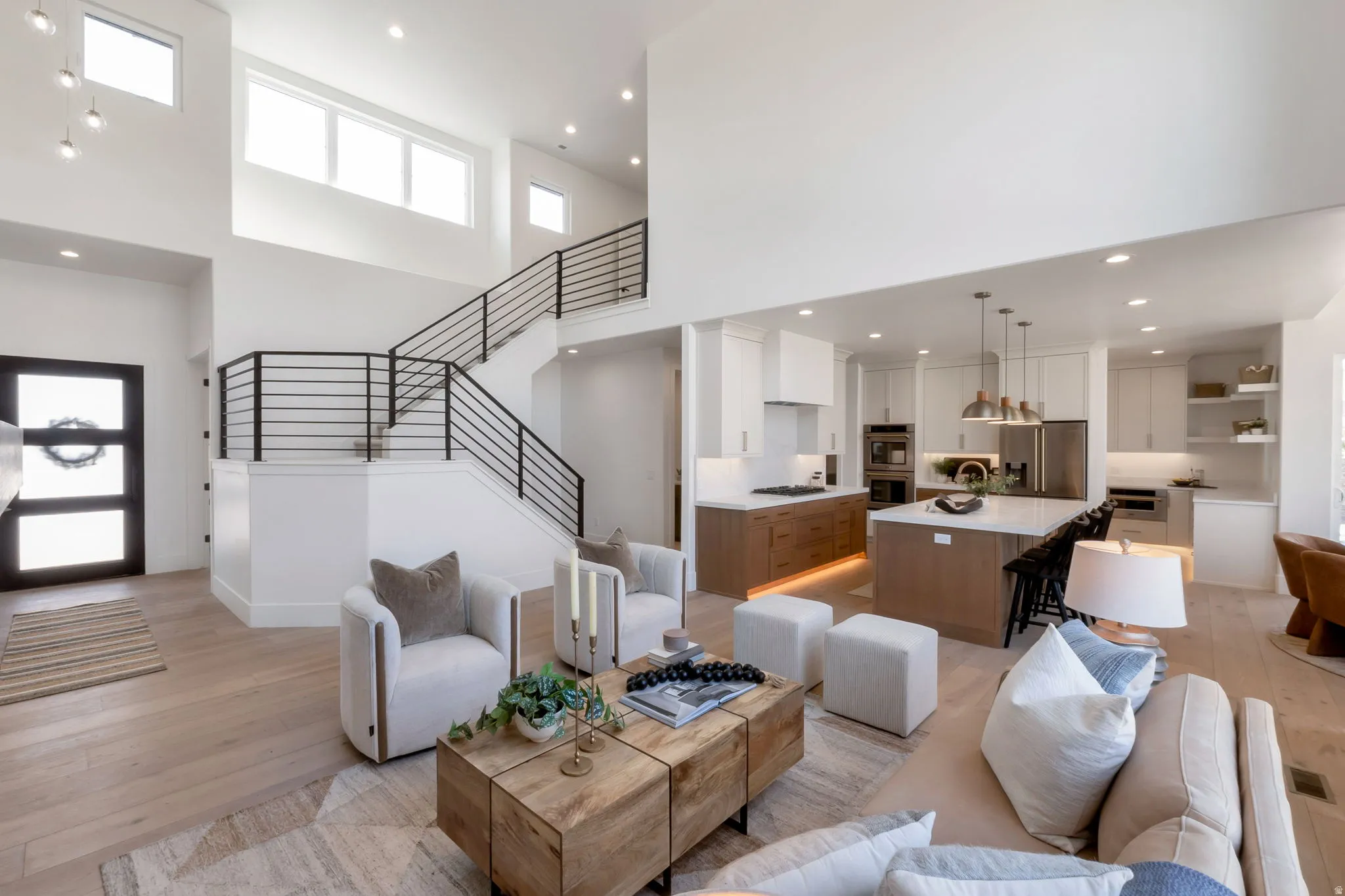 Open-concept living space featuring high ceilings, light wood-finish flooring, and a contemporary staircase with black metal railings