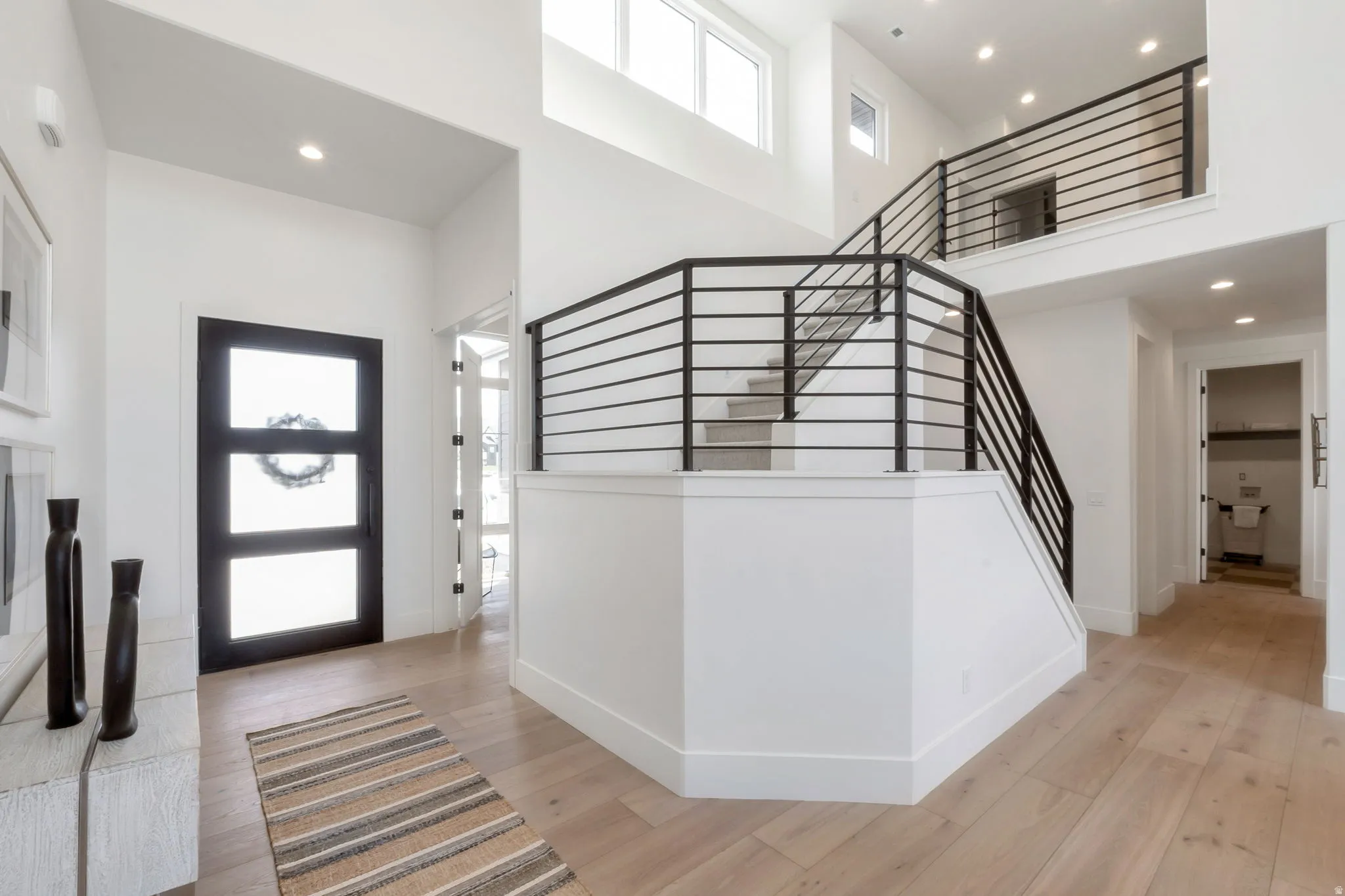 Two-story entry foyer featuring wood-finish flooring, a contemporary staircase with black metal railings, and recessed ceiling lighting