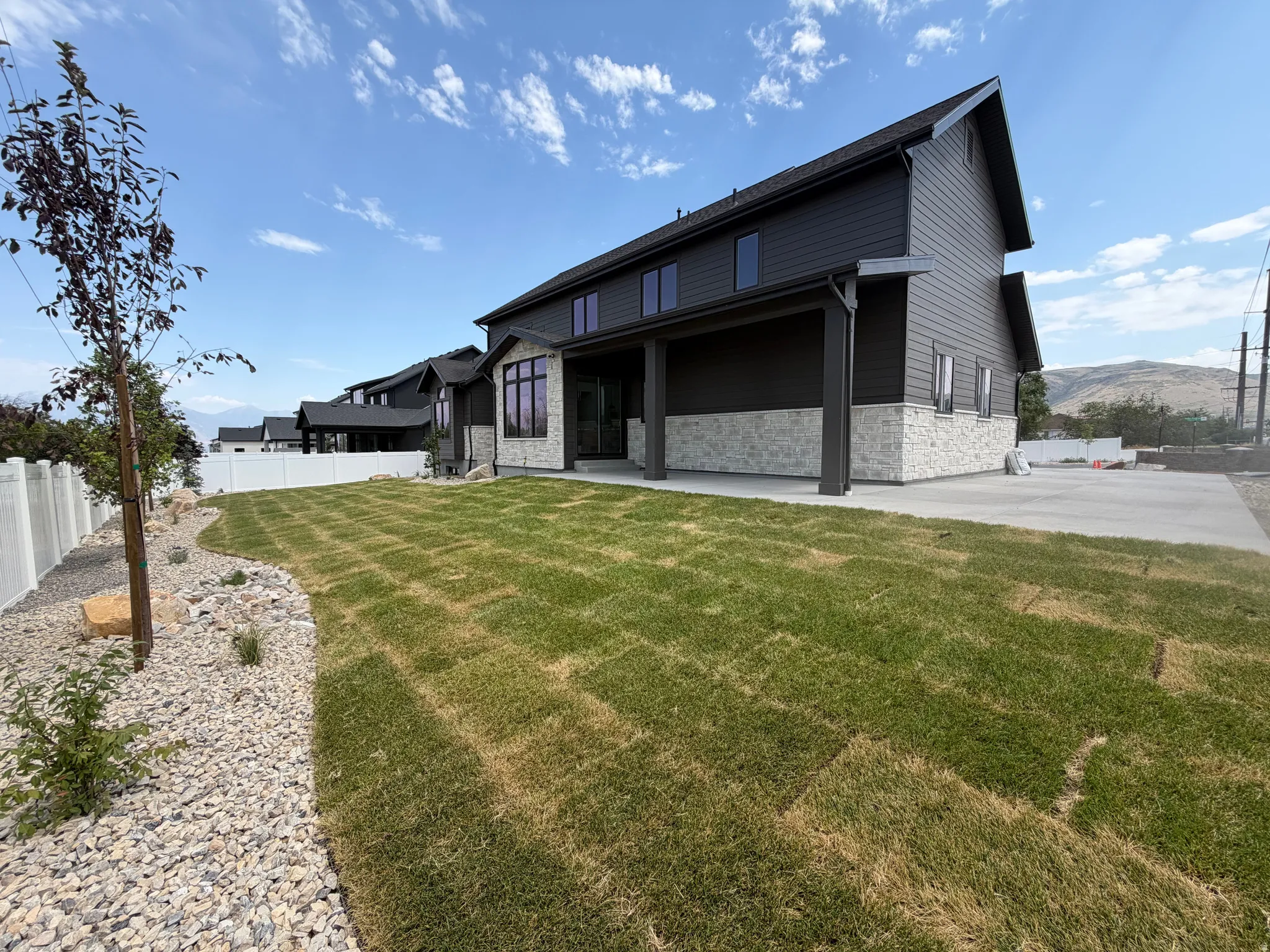 Expansive backyard featuring freshly laid sod, a gravel rock bed, and a young tree