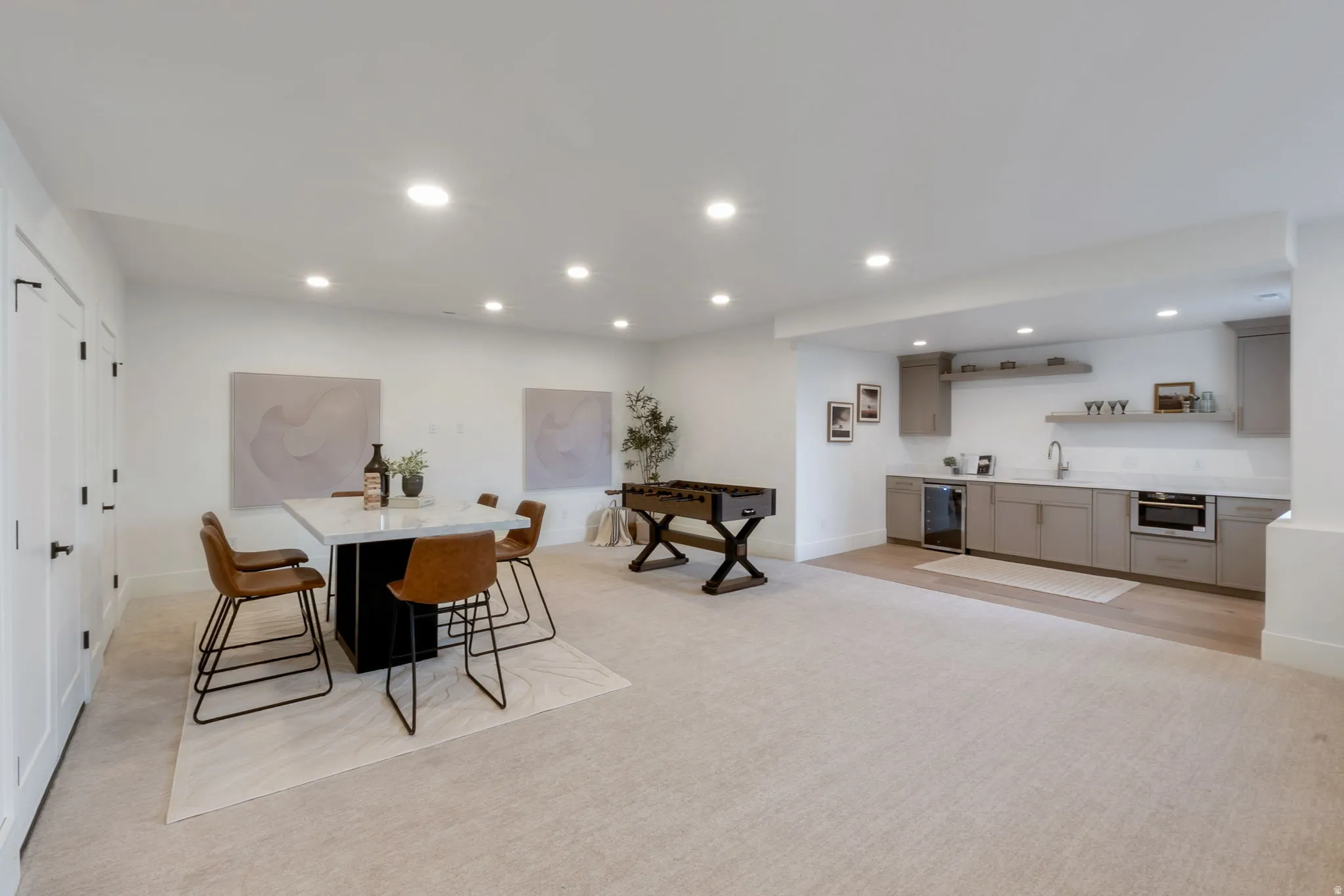 Spacious entertainment area featuring recessed lighting, light-toned carpeting, a built-in wet bar with light cabinetry and open shelving, and wood-finish flooring
