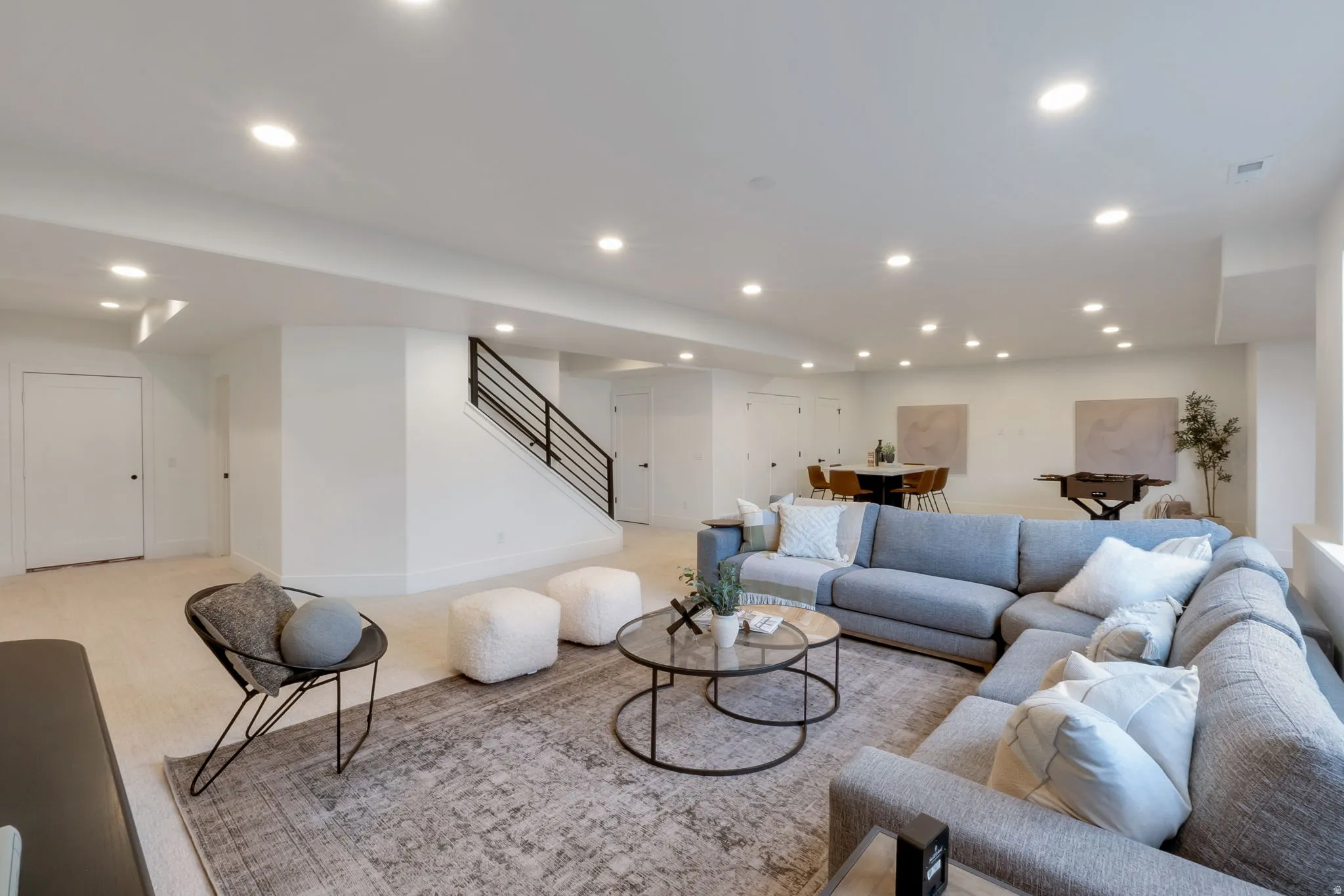 Expansive open-concept room featuring recessed lighting, a contemporary black metal staircase, and light-colored carpeting
