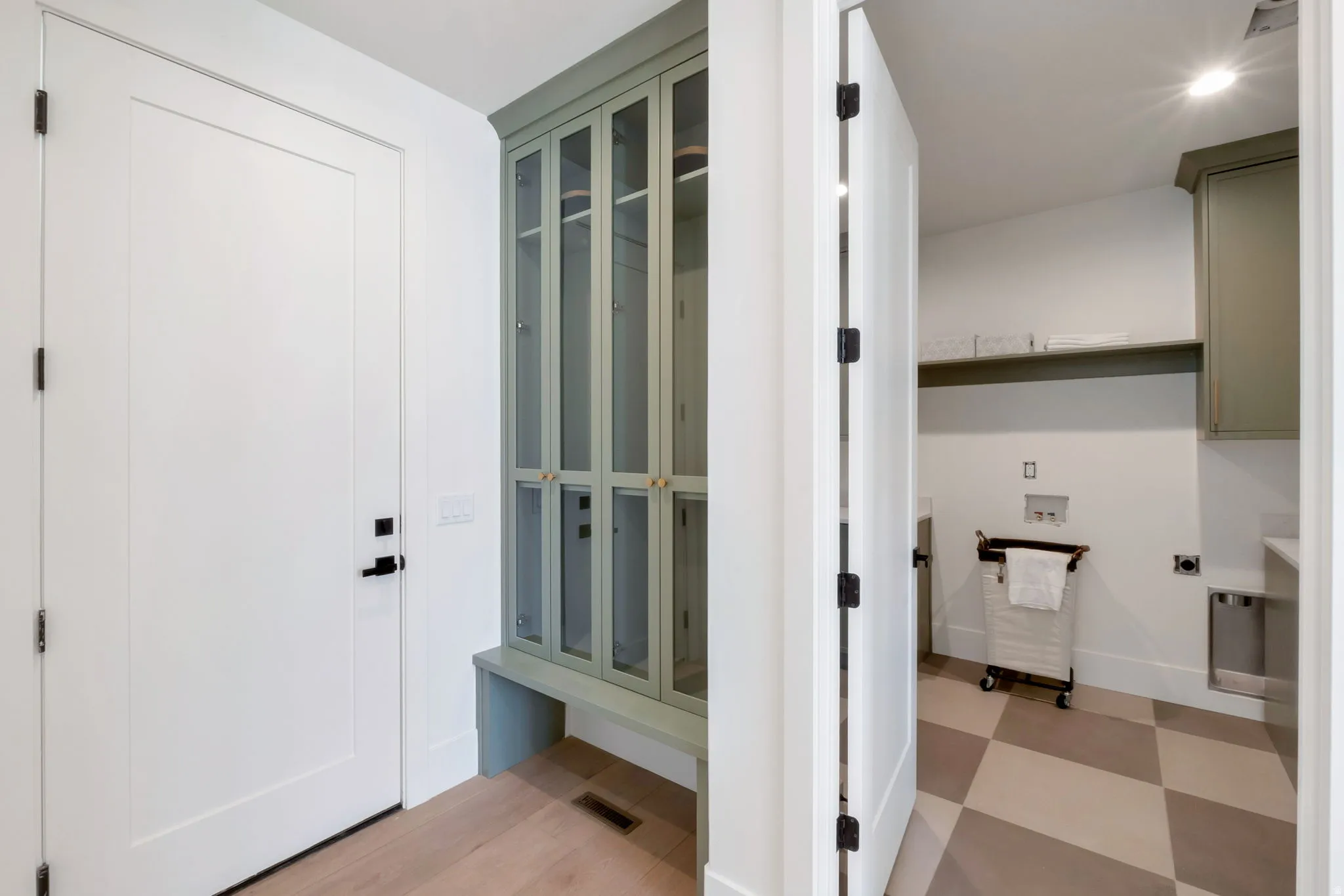 Entryway featuring light wood-finish flooring, a white paneled door with matte black hardware, and a built-in storage cabinet with glass-front doors and bench seating