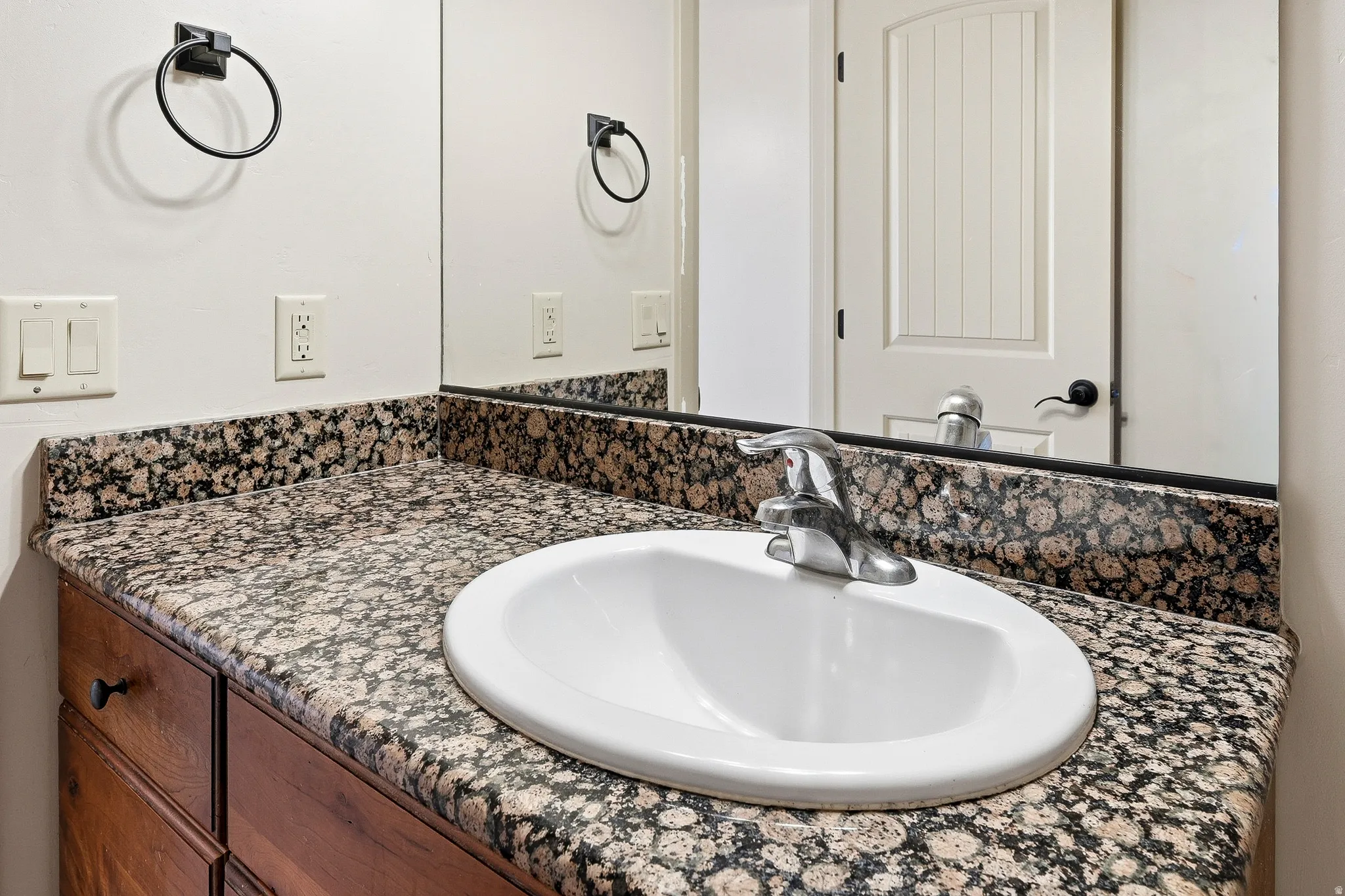 Vanity featuring a polished countertop with integrated sink, wood-finish cabinetry, and chrome faucet