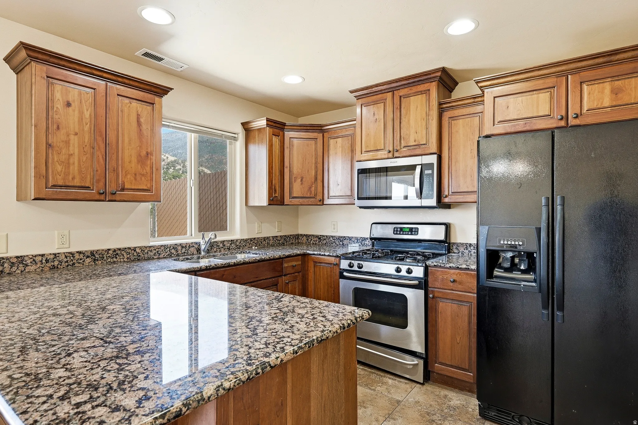 Kitchen with wood cabinetry, granite countertops, stainless steel gas range, built-in microwave, and recessed lighting