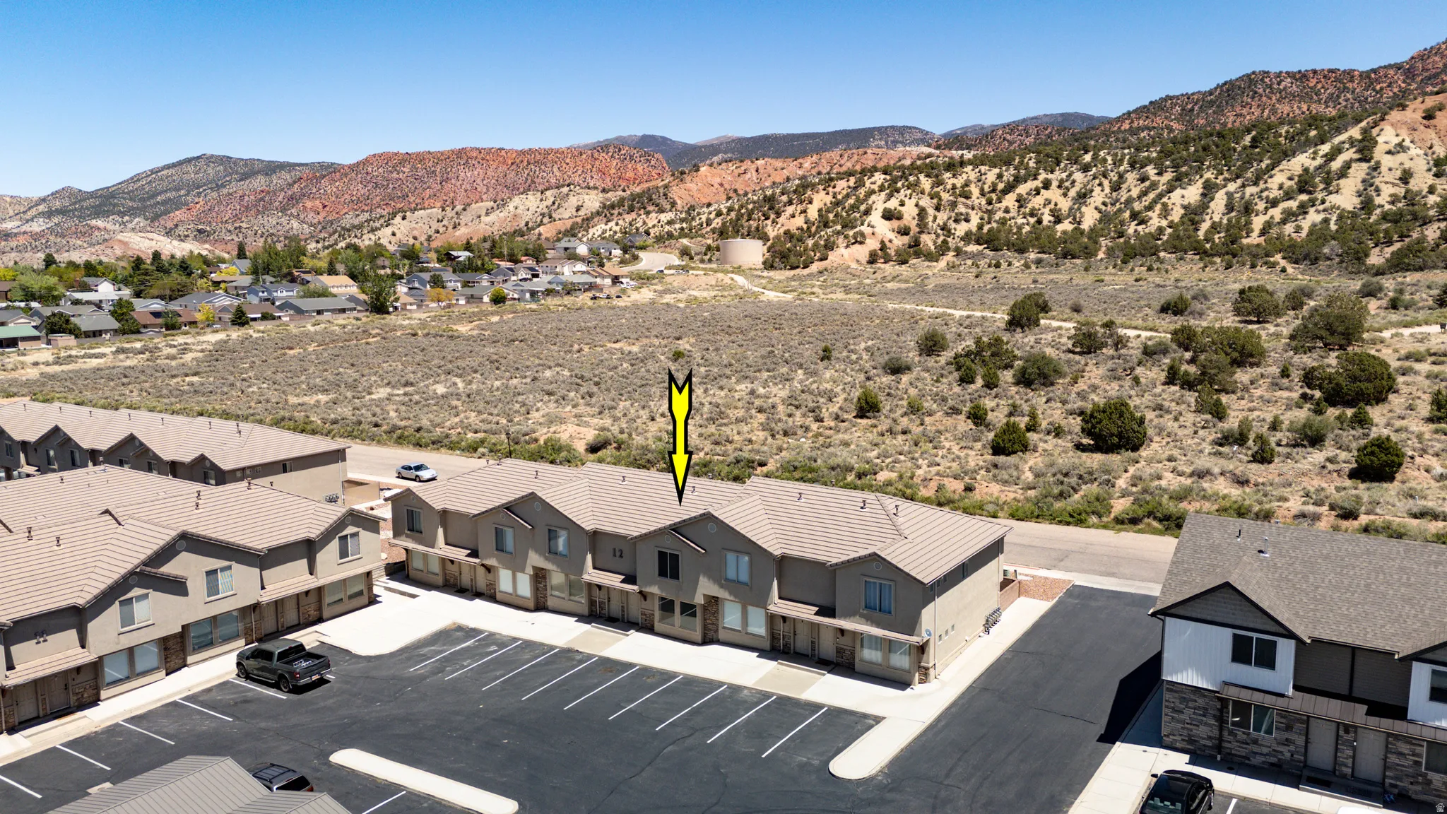 Row of multi-story townhomes featuring neutral-toned exteriors, attached garages, and a shared asphalt parking lot