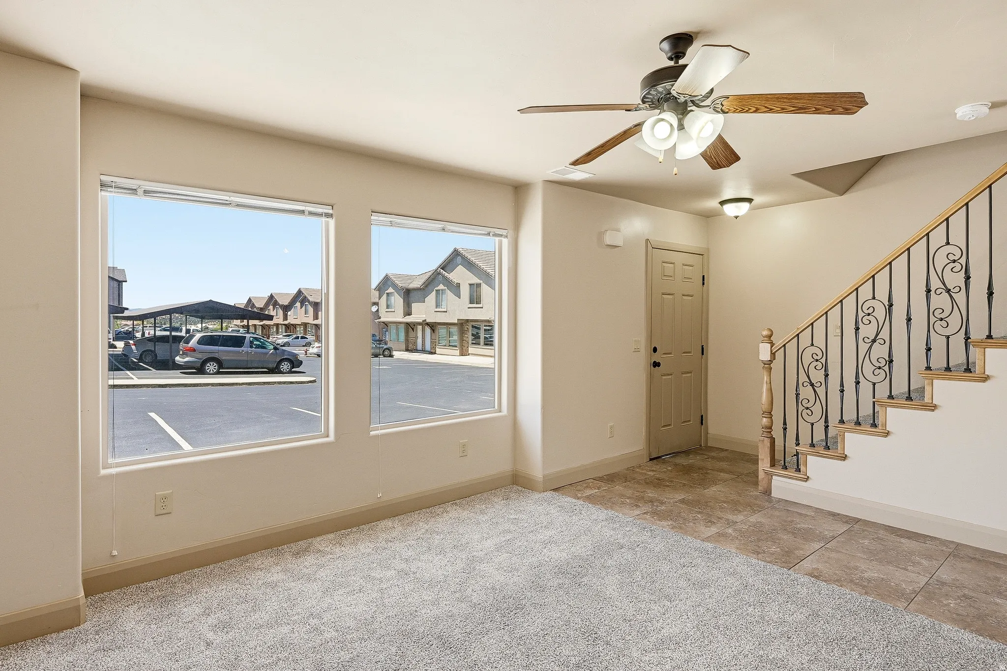 Spacious interior featuring a carpeted living area, tile flooring, and a decorative wrought iron staircase with wood handrail