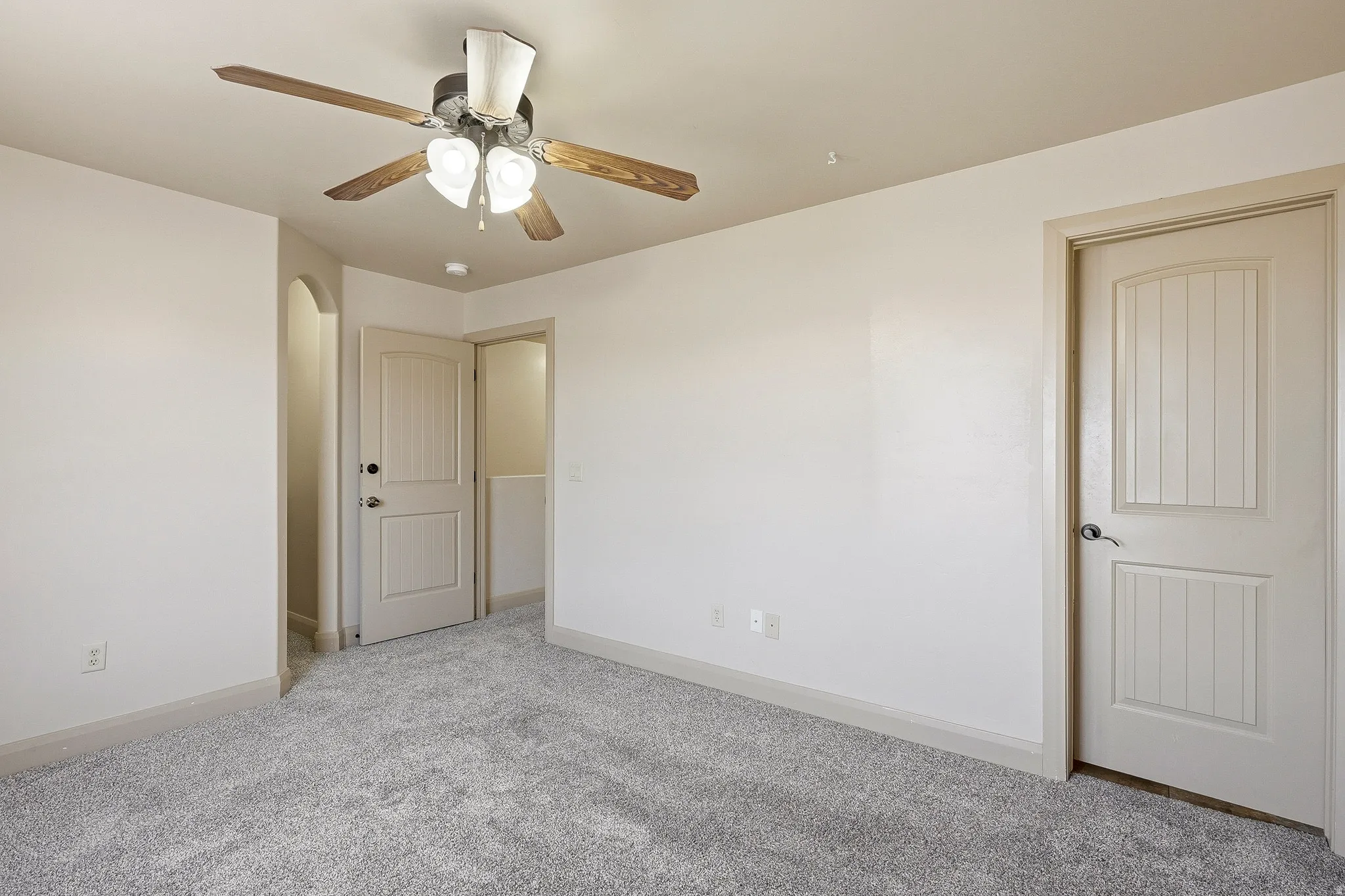 Spacious room featuring light-colored walls and grey carpet flooring