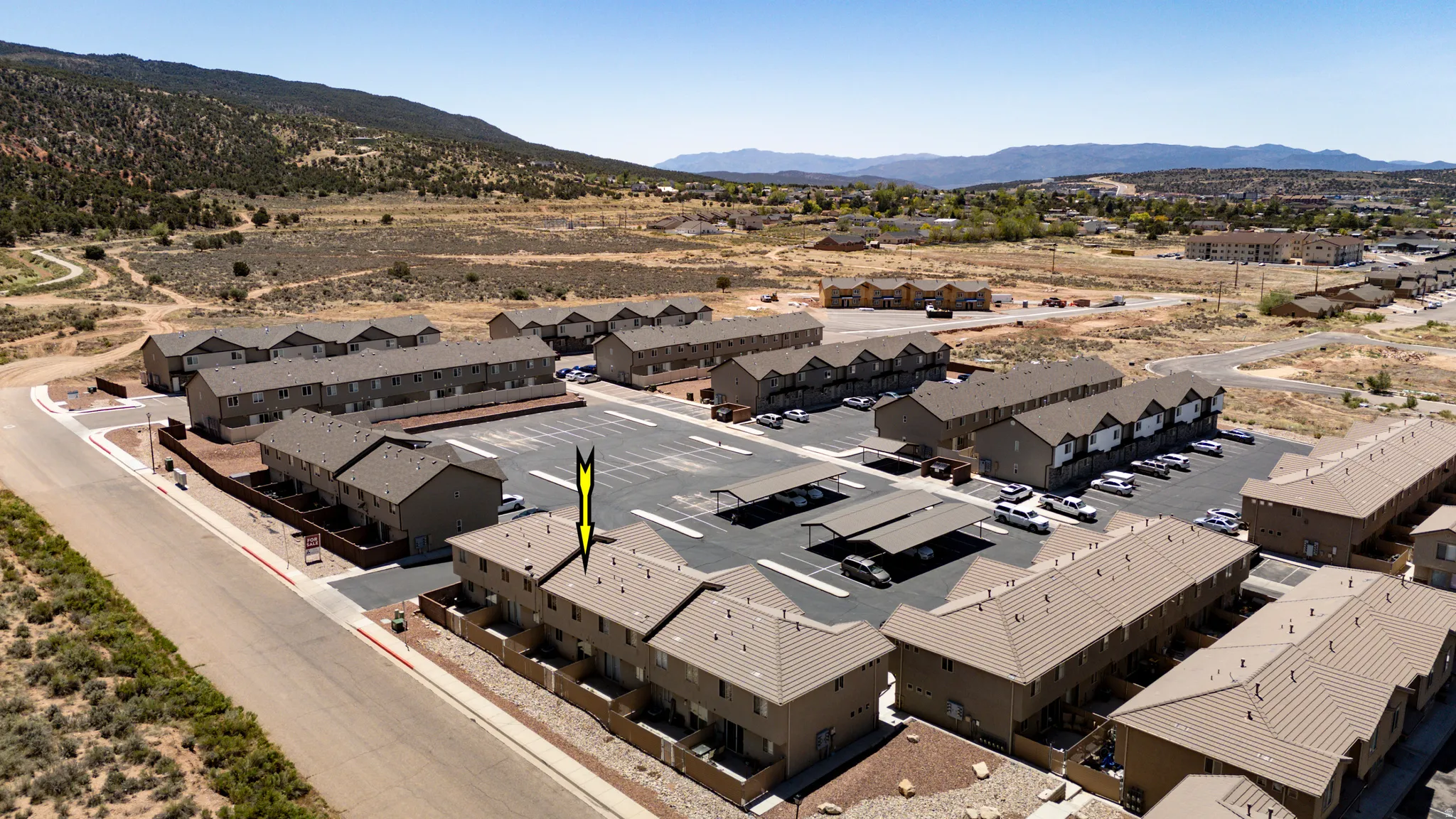 Aerial perspective of a multi-unit property featuring rows of townhome-style buildings, extensive paved parking areas, and covered parking structures