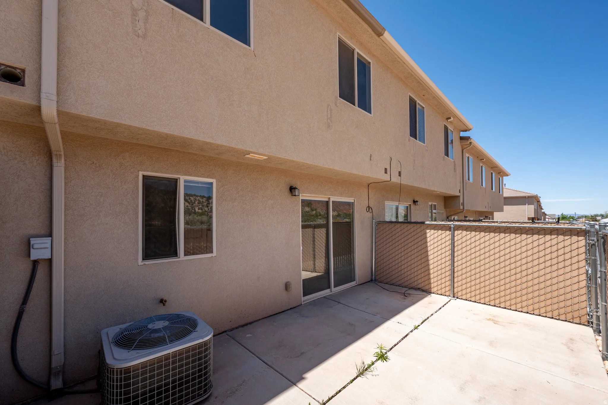 Concrete patio with sliding glass doors, stucco exterior, and chain-link fencing with privacy screening