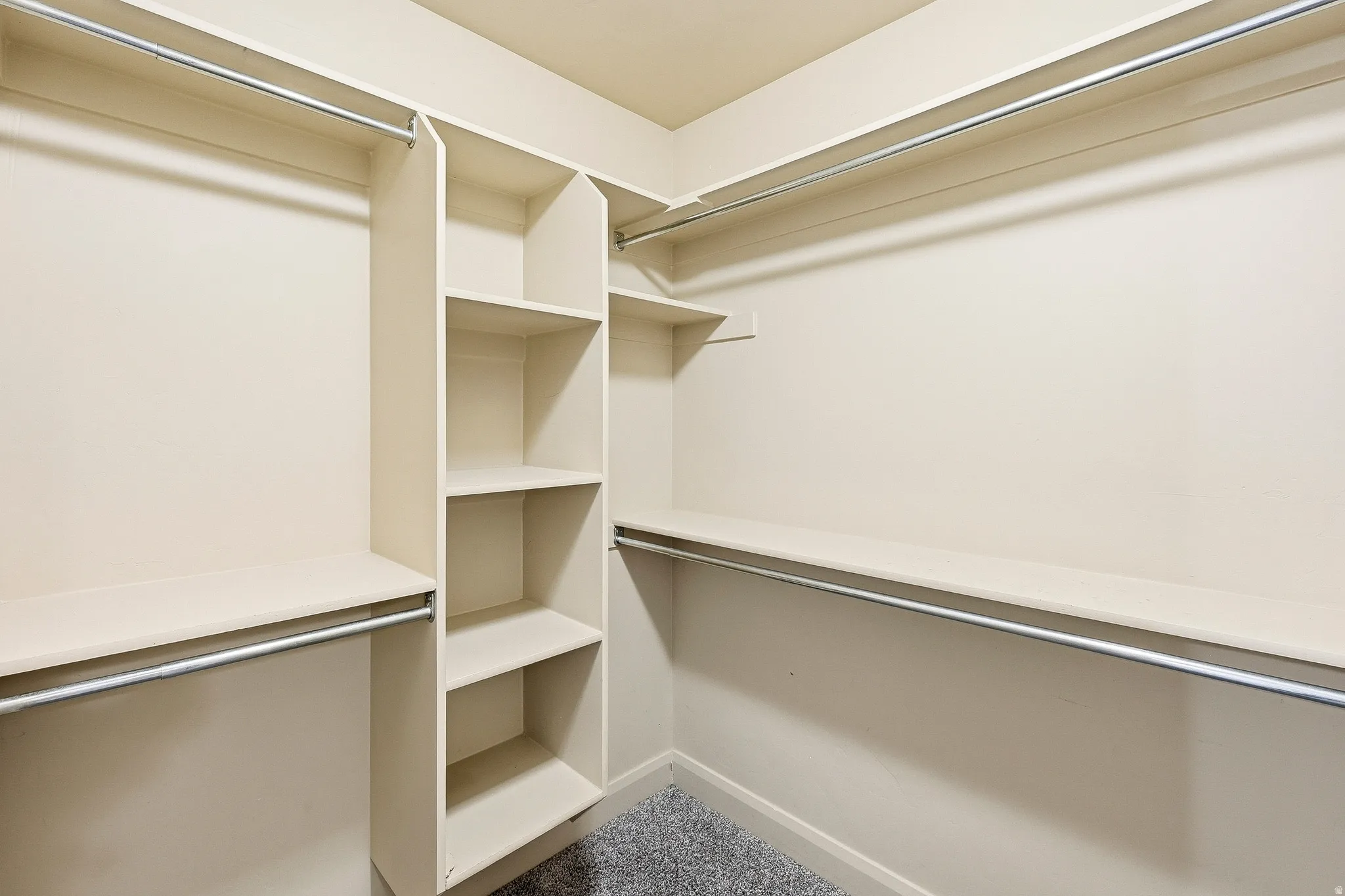 Walk-in closet with integrated shelving units, multiple hanging rods, and light-colored walls