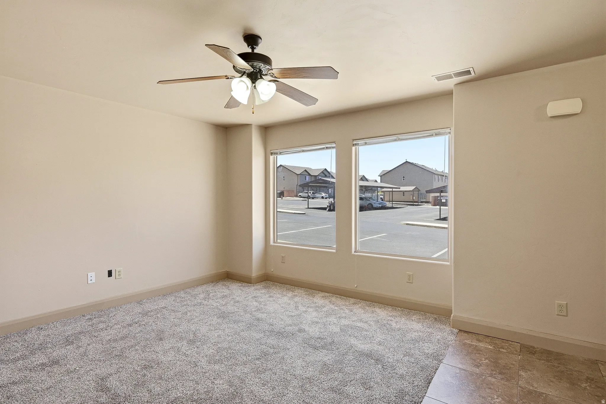 Neutral-toned room featuring a ceiling fan with integrated lighting, two large windows, plush gray carpeting, and beige wall paint