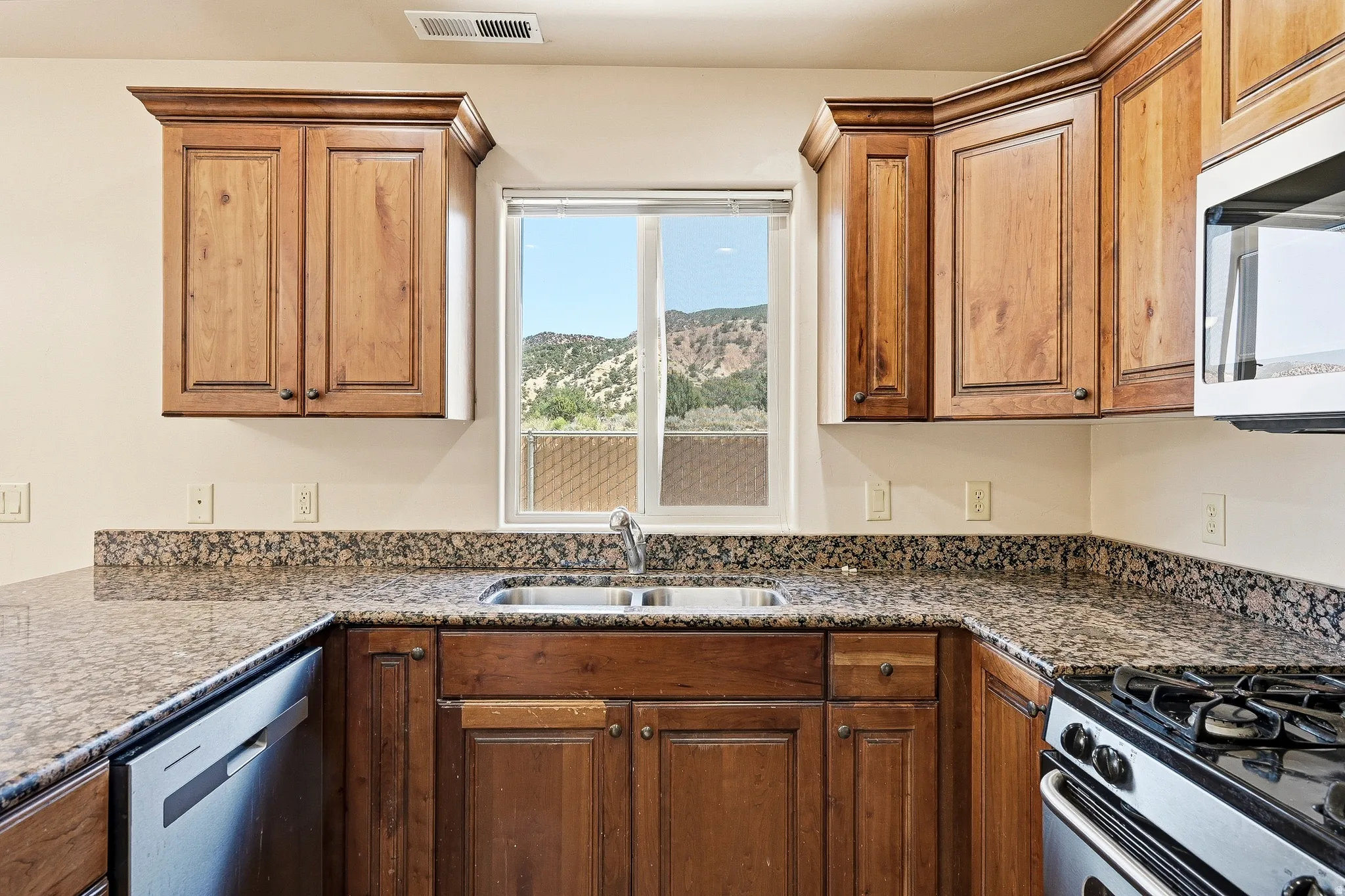 Kitchen featuring wood cabinetry, speckled countertops, stainless steel sink, and stainless steel dishwasher
