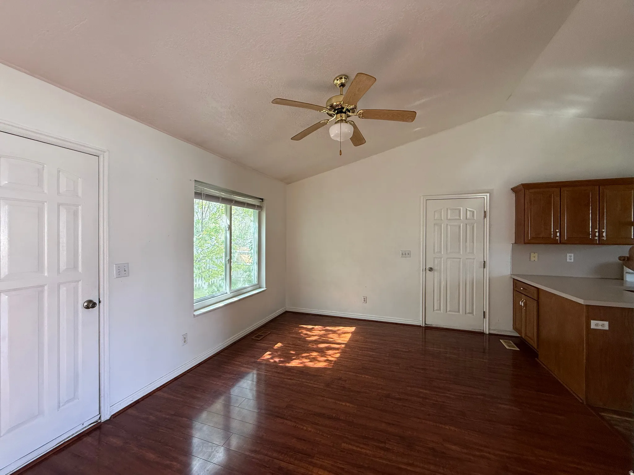 Vaulted ceilings with a ceiling fan, wood-finish flooring, white paneled doors, a window with horizontal blinds, and wood cabinetry with a light-colored countertop