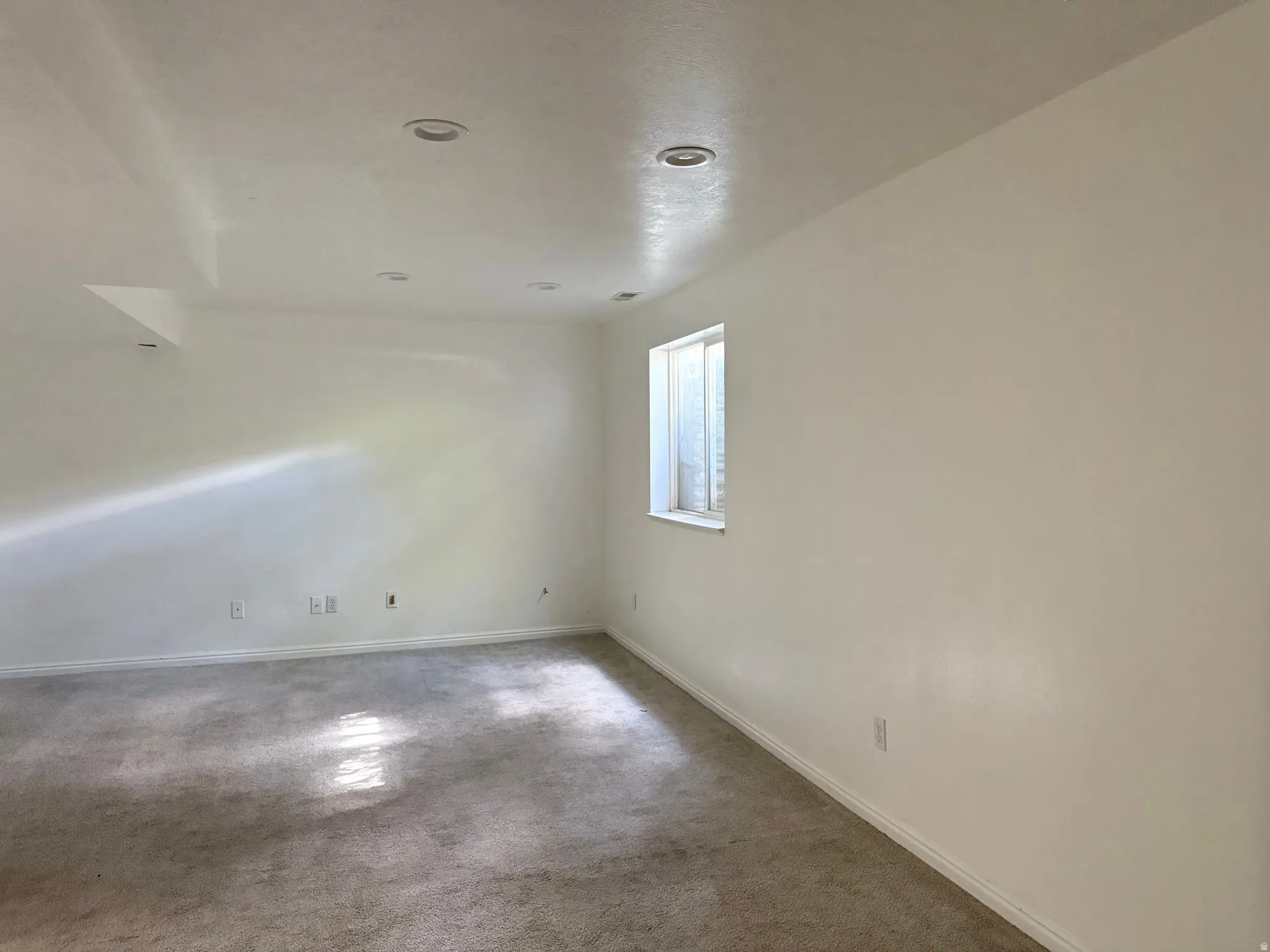 Spacious room featuring neutral carpeting, a single window, white walls, and recessed ceiling lighting