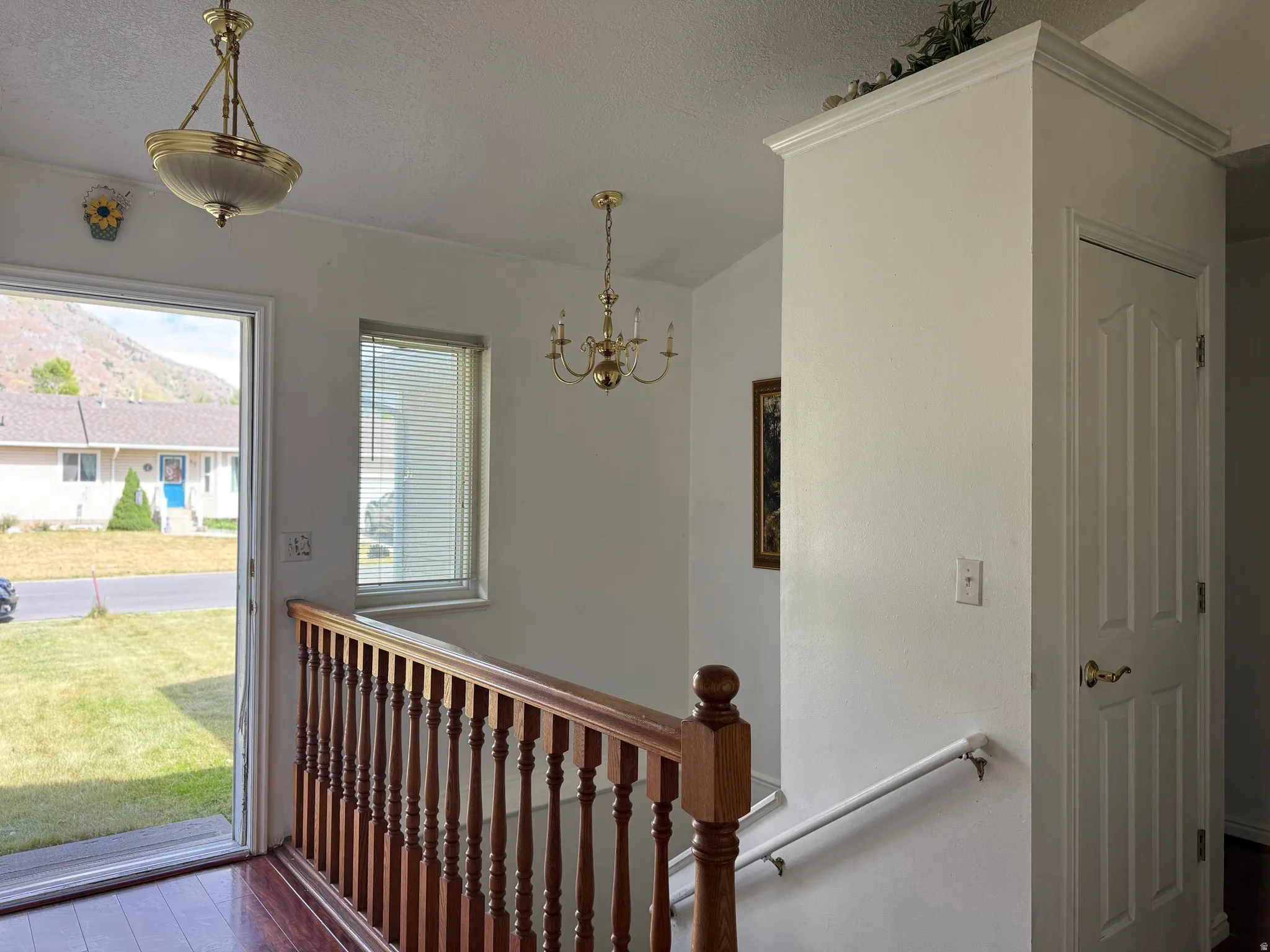 Entryway featuring wood-finish flooring, a traditional wood staircase railing, and a brass-finish chandelier