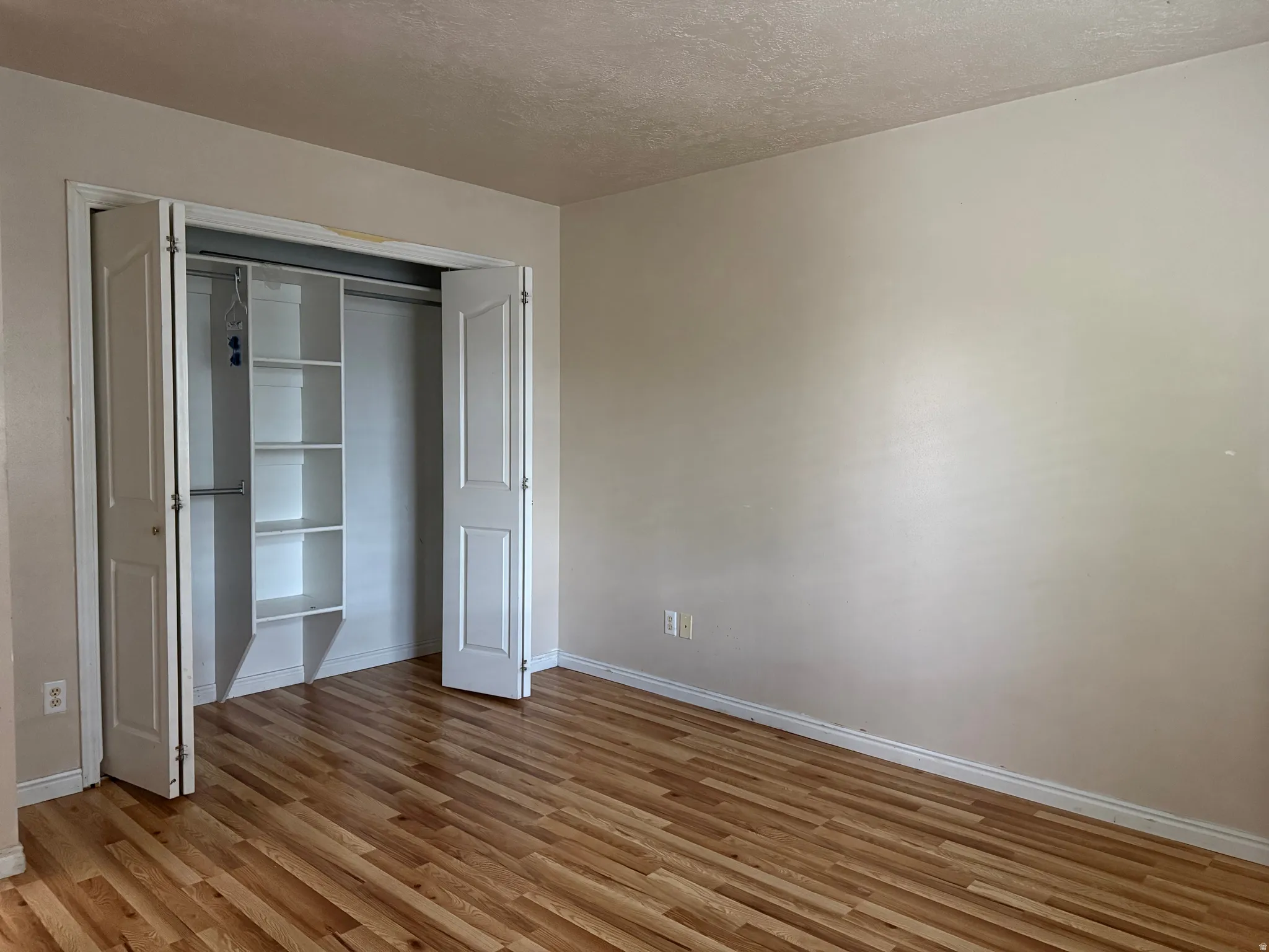 Room featuring wood-finish flooring, light-toned walls, and a closet with bifold doors