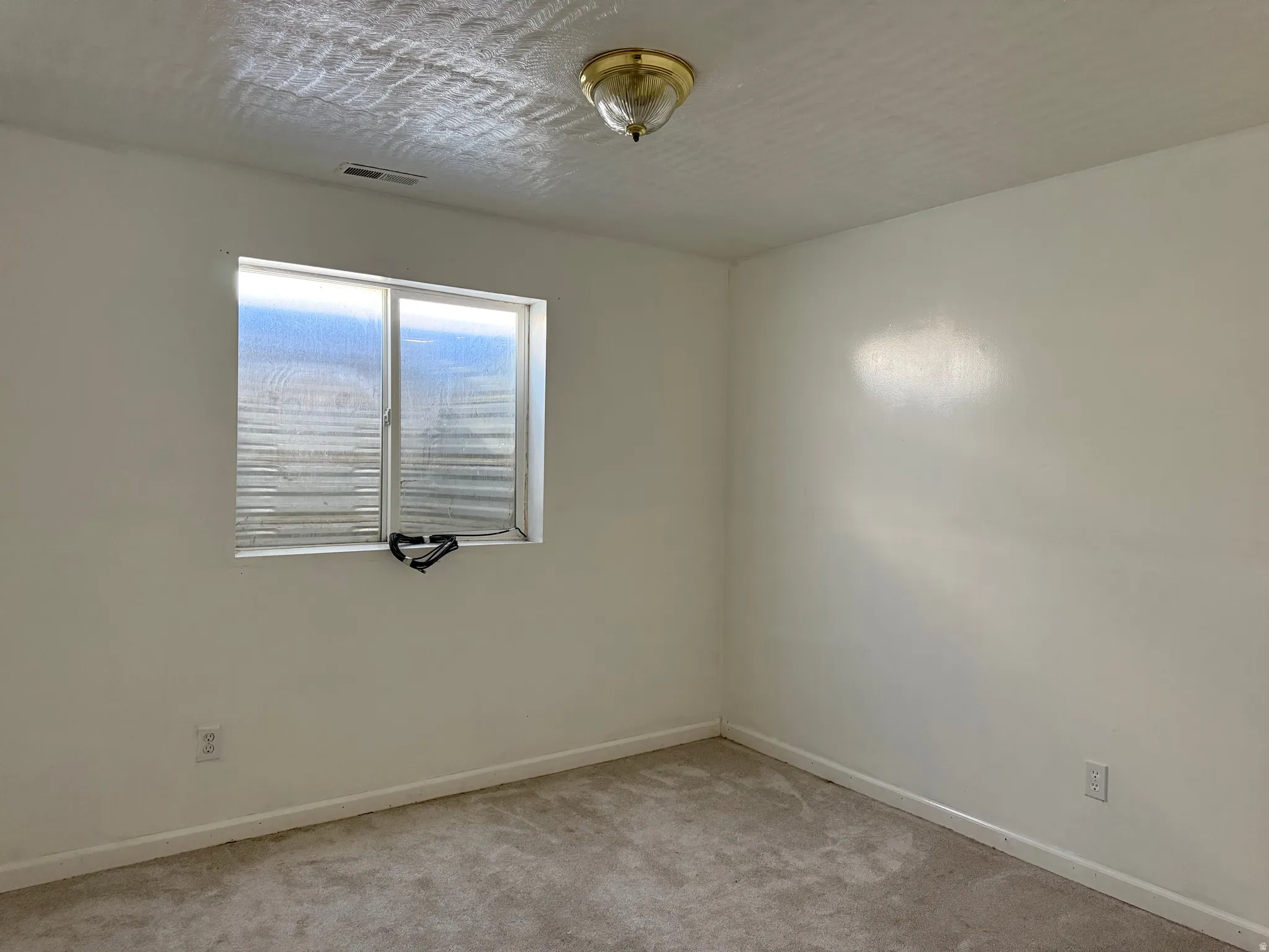 Room featuring a single window, light-colored walls, and a textured ceiling